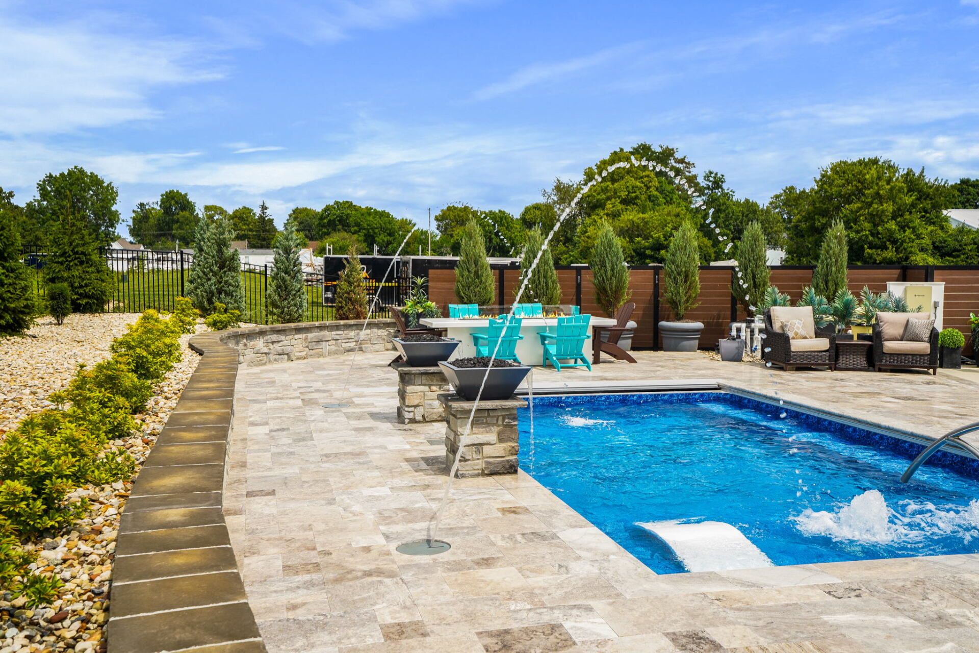 Backyard pool with stone deck, lounge chairs, and turquoise water surrounded by greenery