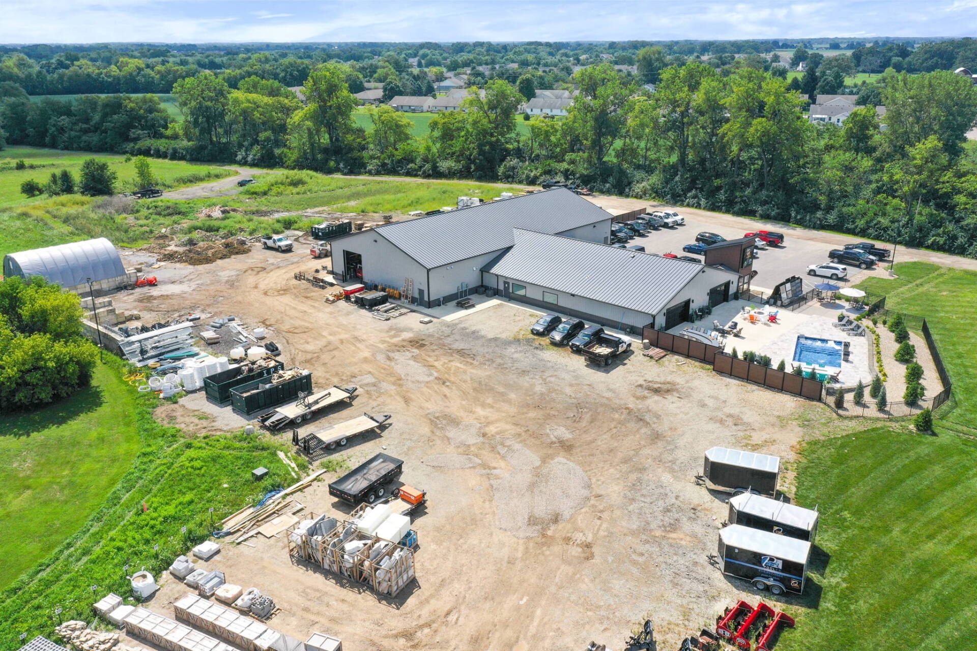 Aerial view of a large industrial yard with buildings, trucks, and equipment surrounded by green fields.