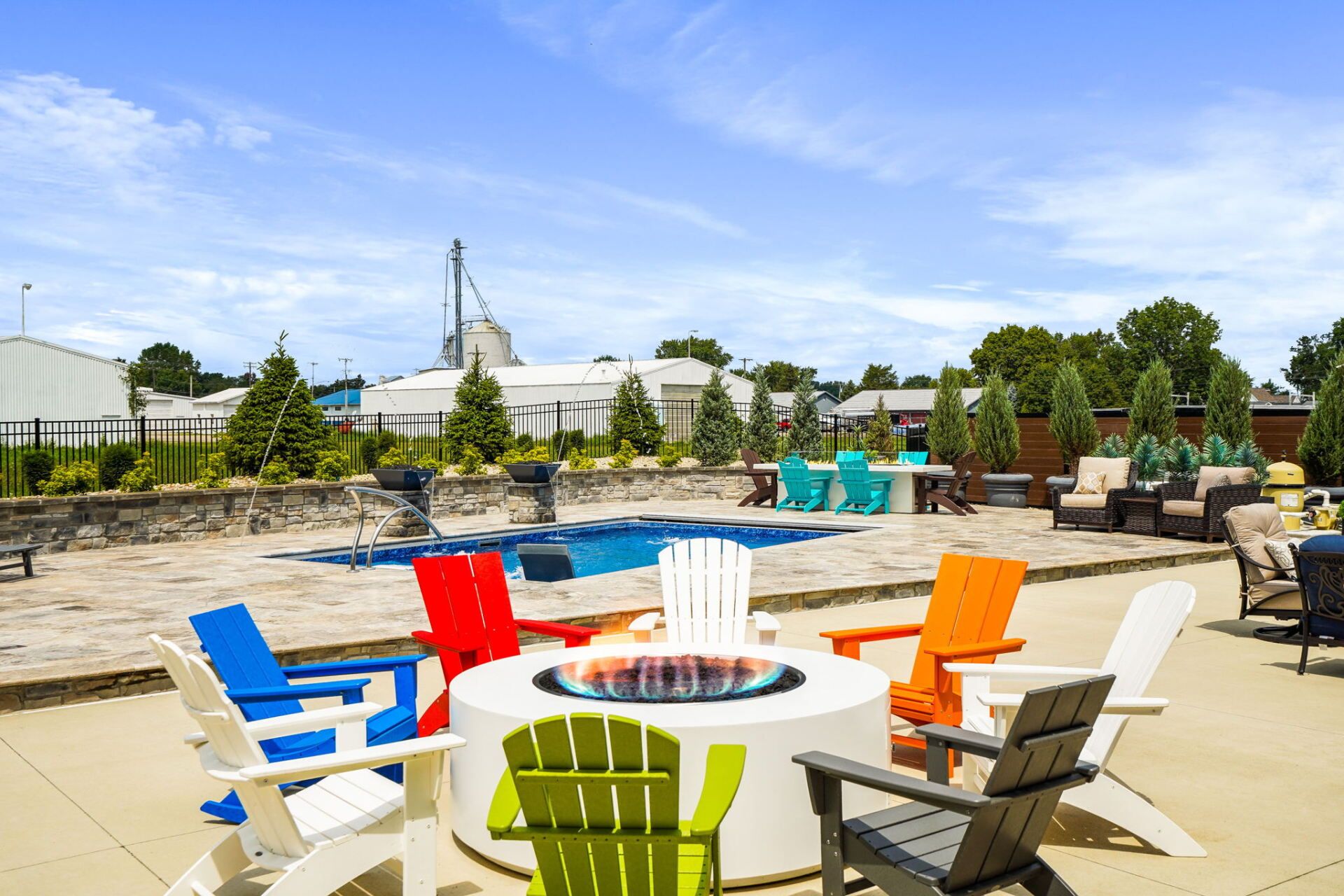Colorful chairs around a fire pit on a sunny rooftop patio with stone seating and trees in the background
