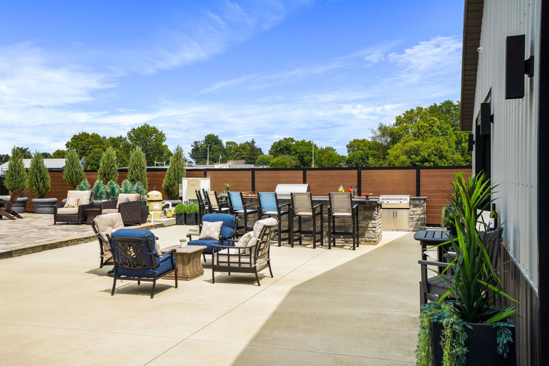 Outdoor patio with lounge chairs, tables, and potted plants under a blue sky