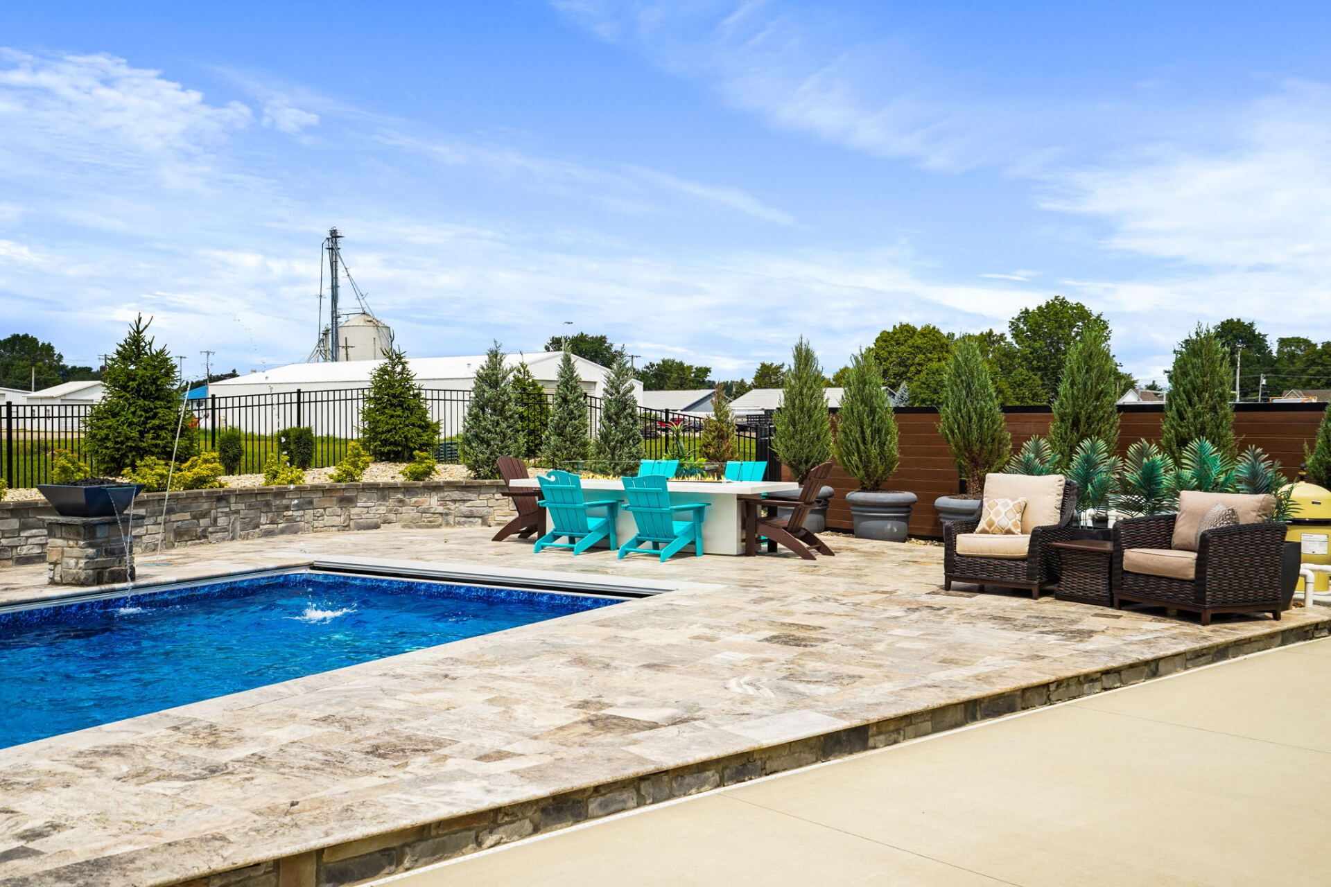 Backyard pool with stone patio, turquoise chairs, and outdoor seating under a blue sky