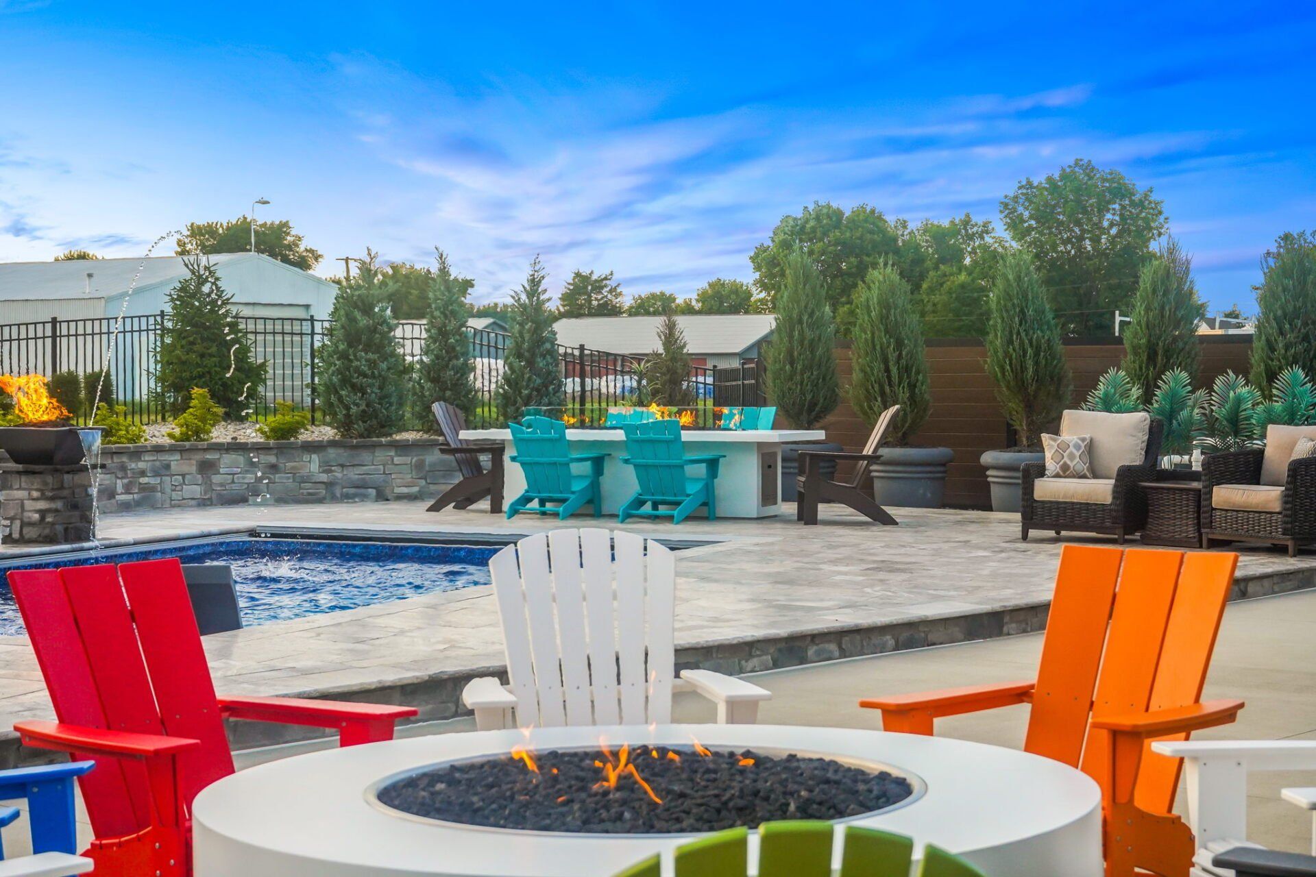 Colorful patio chairs around a fire pit beside a pool on a sunny outdoor deck