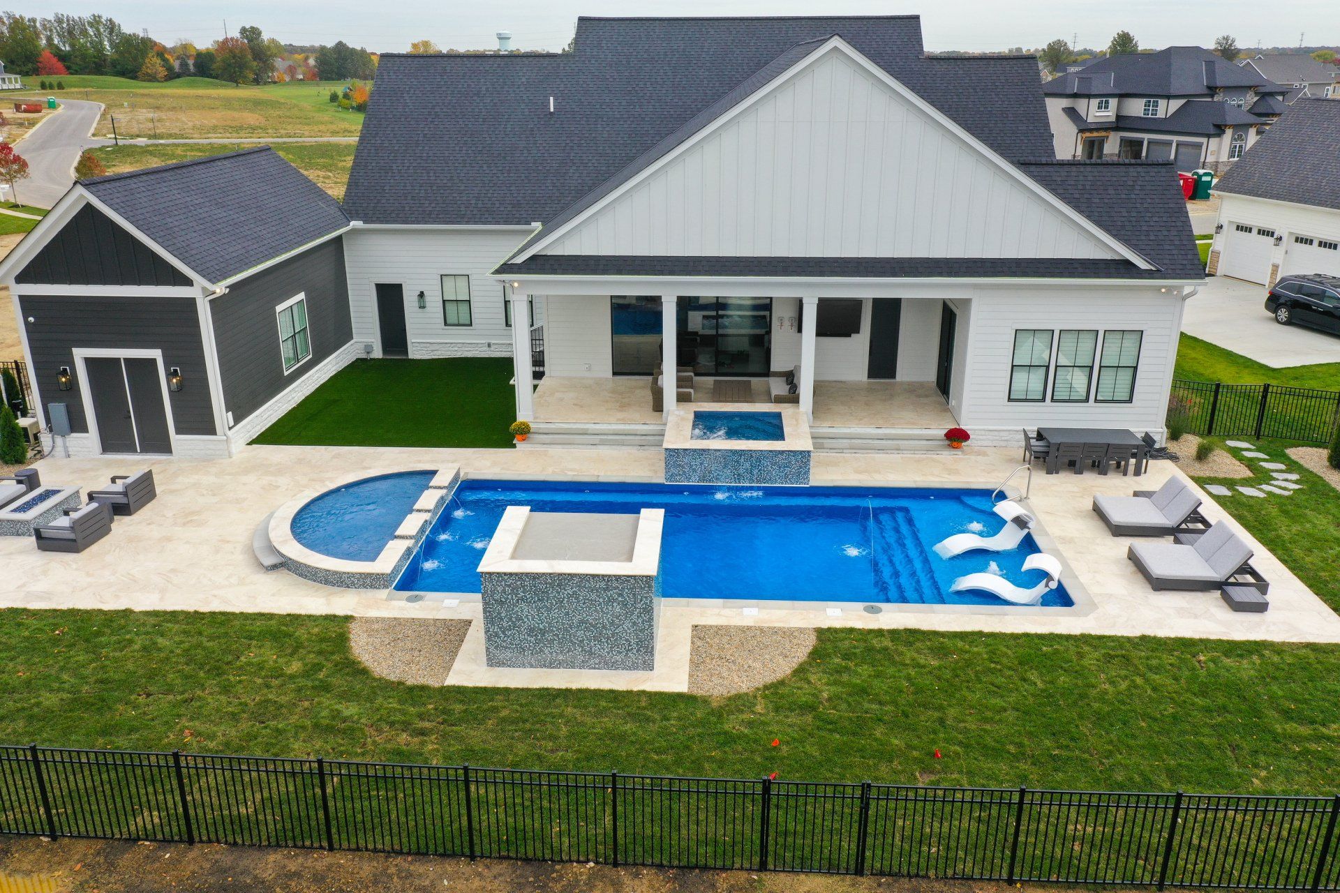 Modern house with a blue backyard pool, patio lounge chairs, and a small gazebo by a fenced lawn