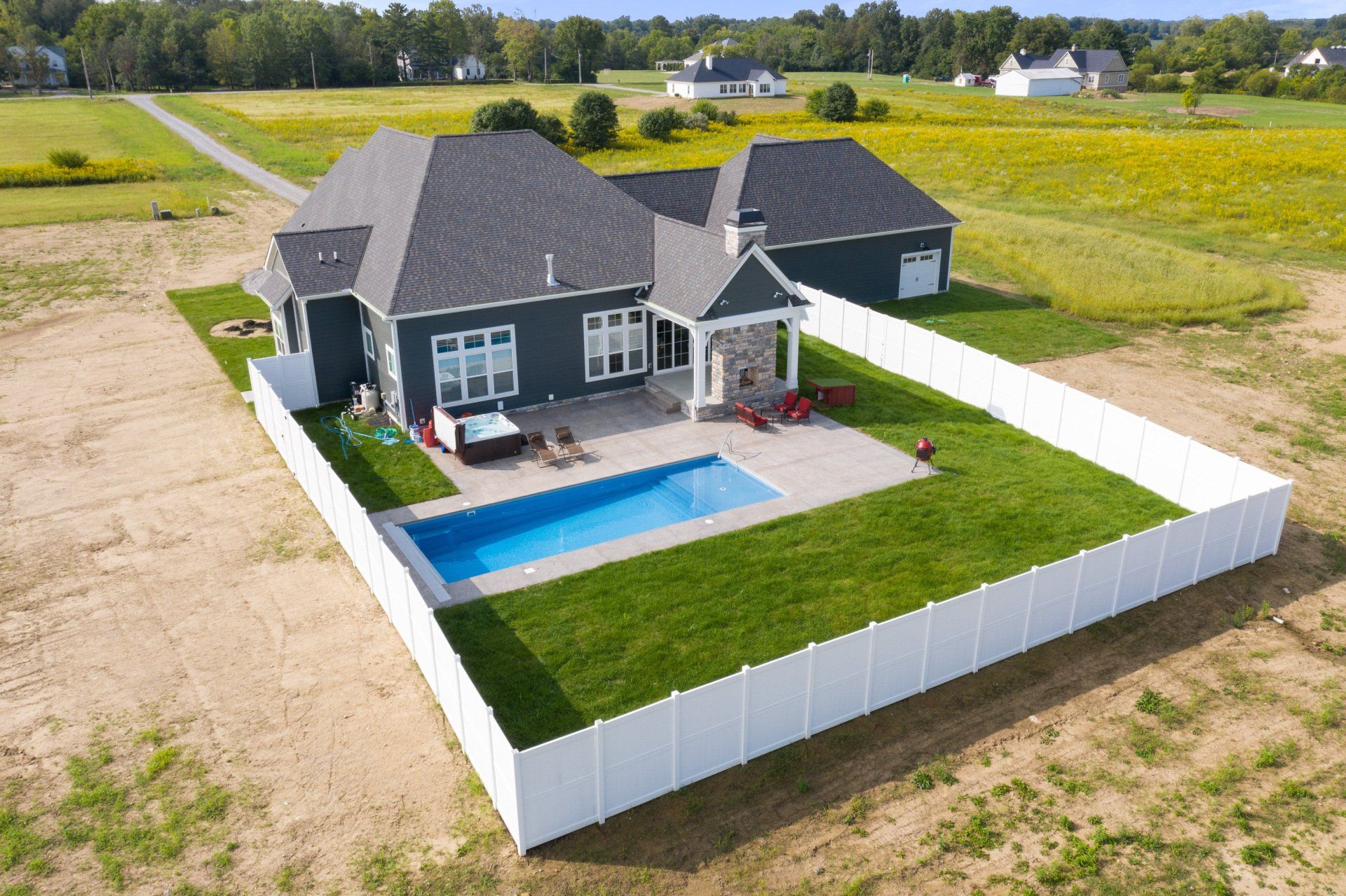 Aerial view of a modern house with a fenced backyard, blue pool, and green lawn in a rural field setting