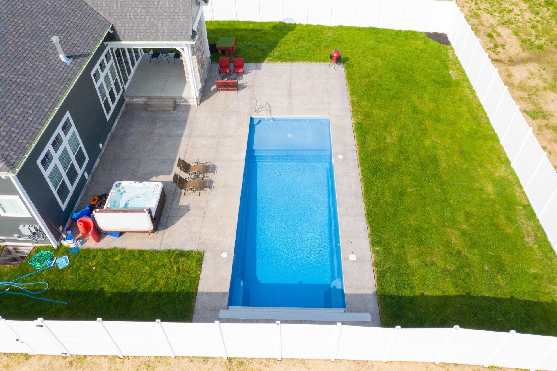 Aerial view of a backyard with a rectangular pool, patio furniture, and green lawn beside a house.