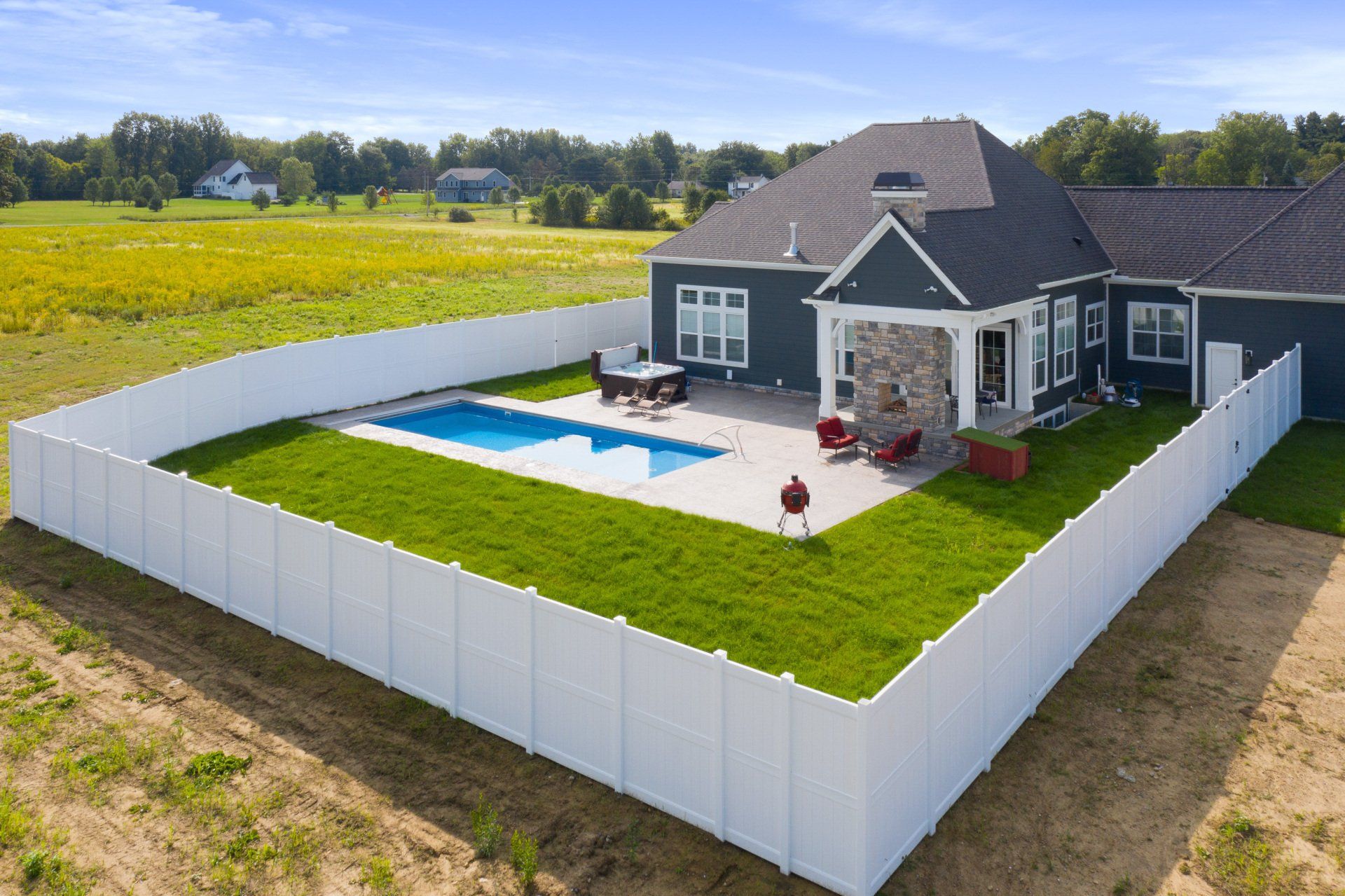 Aerial view of a fenced backyard with a house, swimming pool, white deck, and green lawn.