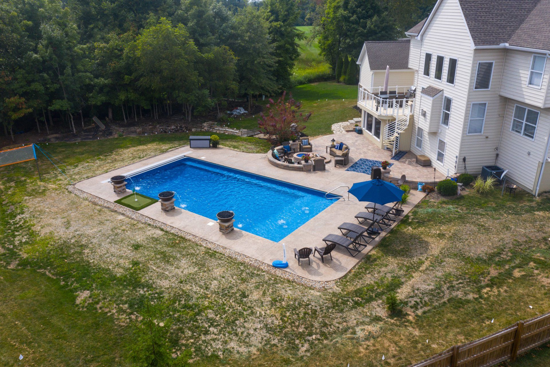 Aerial view of a house with a backyard swimming pool, patio, lounge chairs, and surrounding trees.