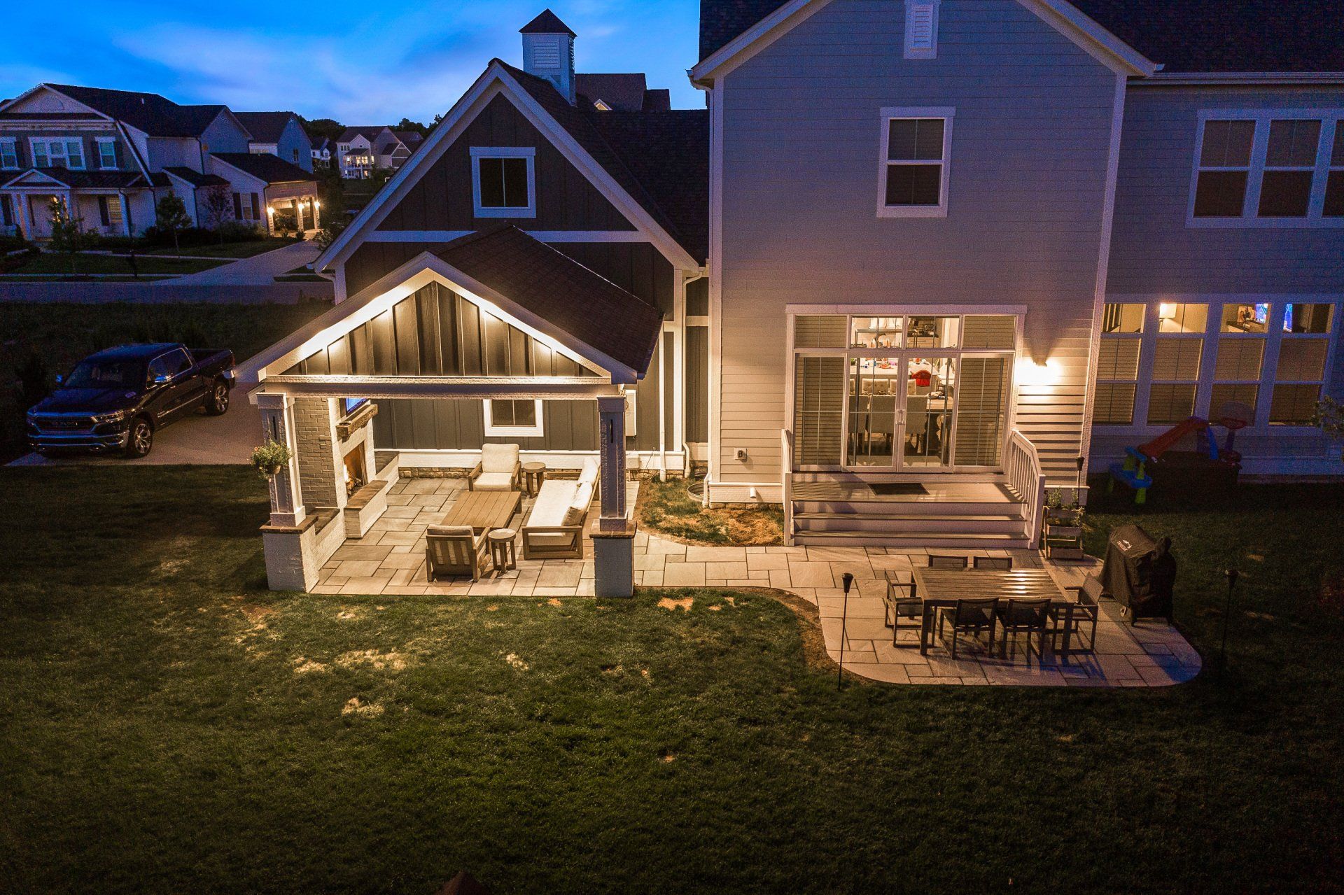 Backyard patio at dusk with lit gazebo, two-story house, and outdoor dining table