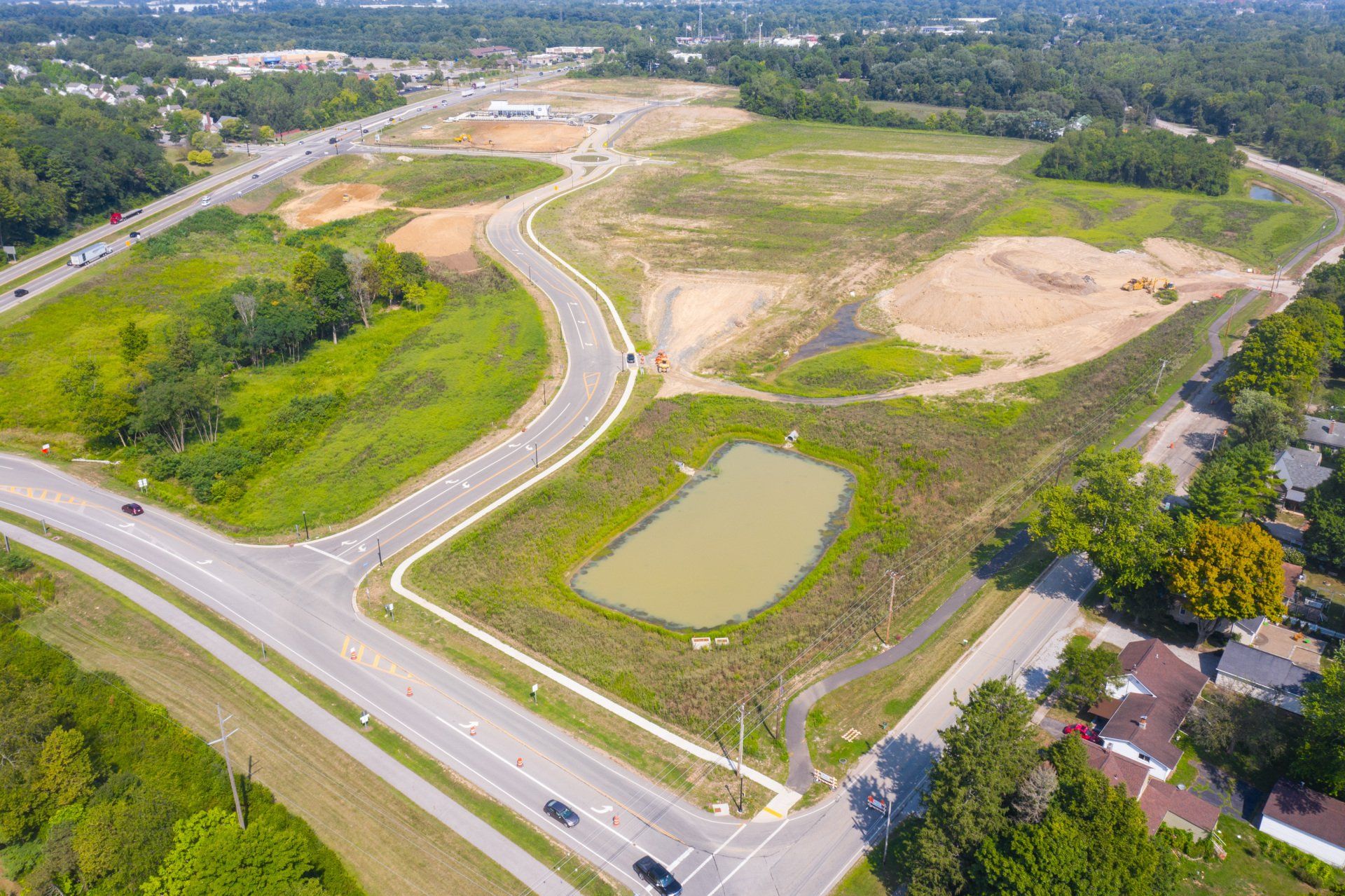Aerial view of a curving road beside a pond and empty construction lots in a suburban area