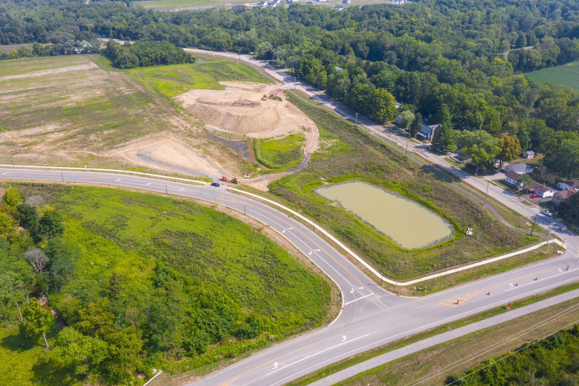 Aerial view of a rural road intersection beside green fields and a wooded area