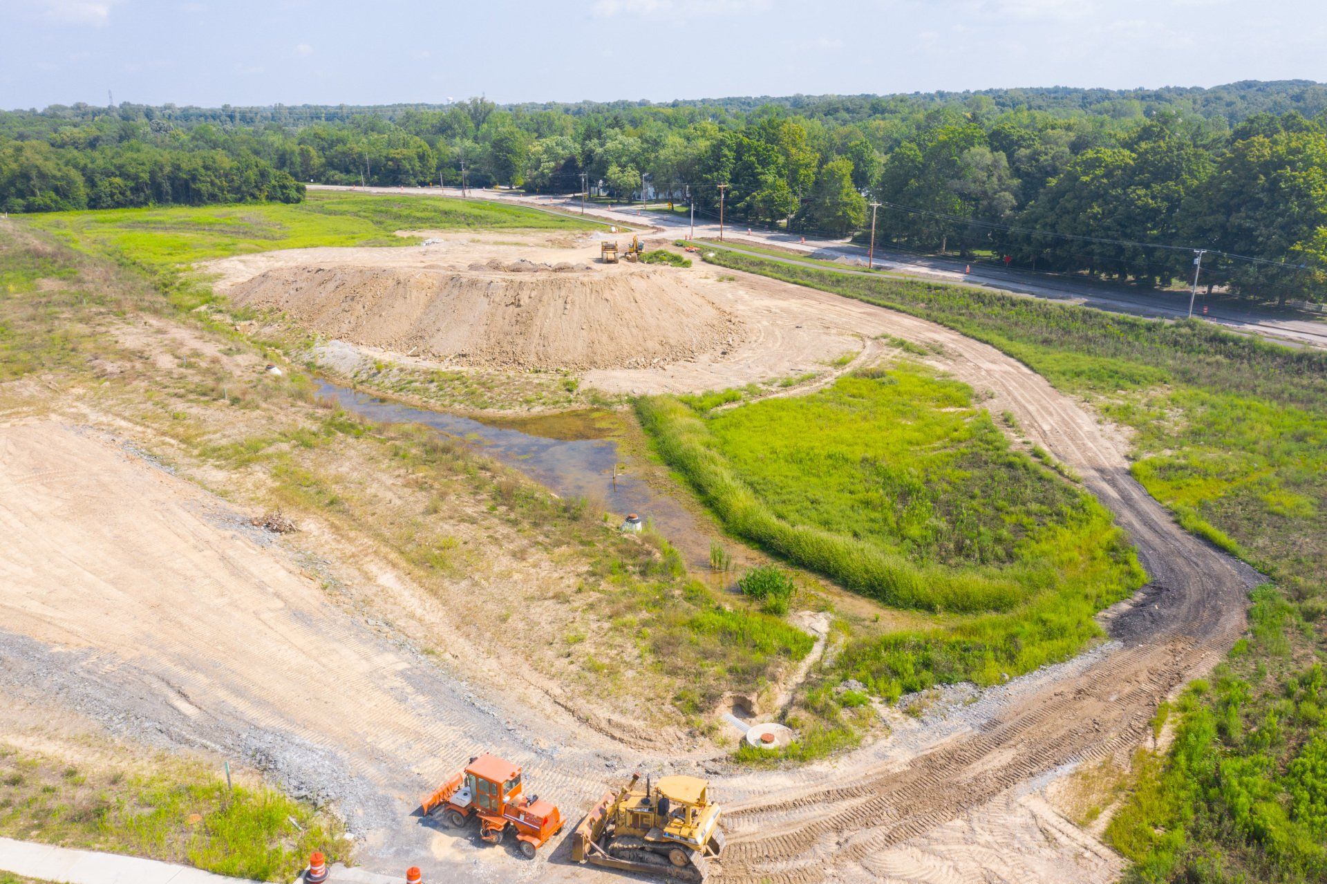 Aerial view of a large dirt construction site with winding roads and green trees nearby