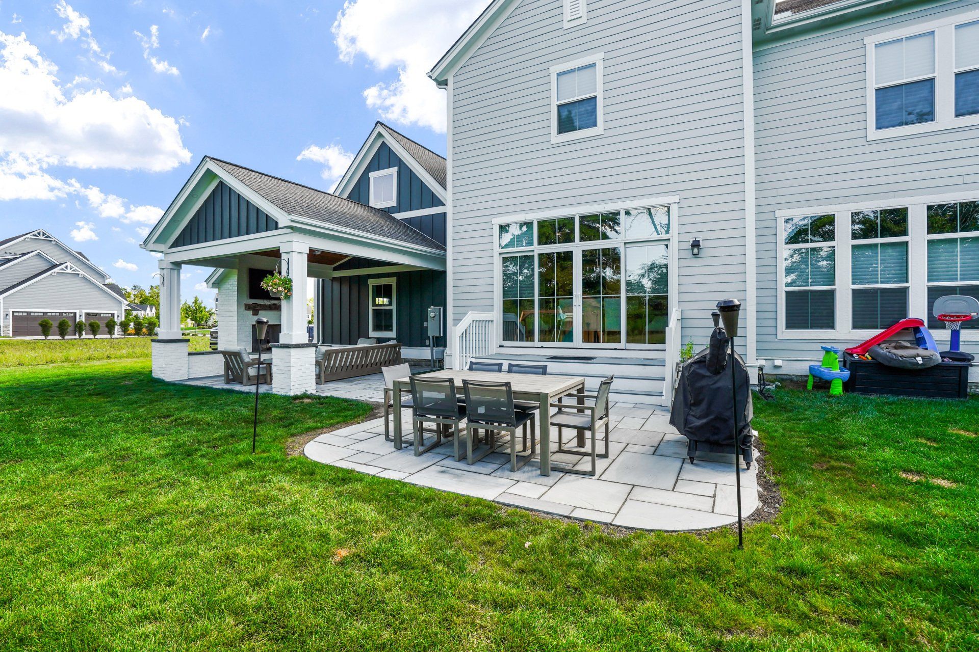 Backyard patio with outdoor dining set and grill beside a gray house on a green lawn