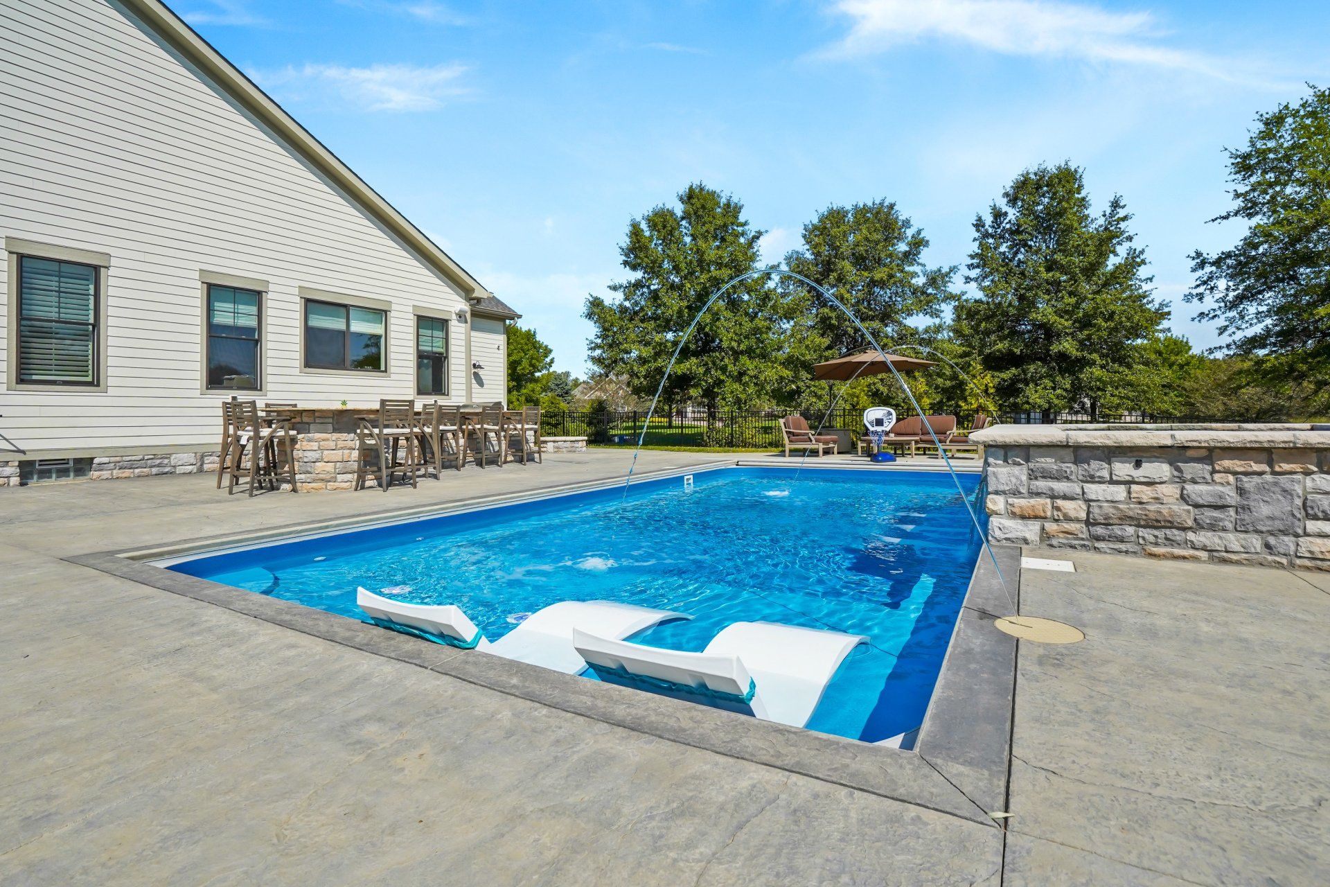 Outdoor swimming pool beside a white building, with lounge chairs and trees under a clear blue sky