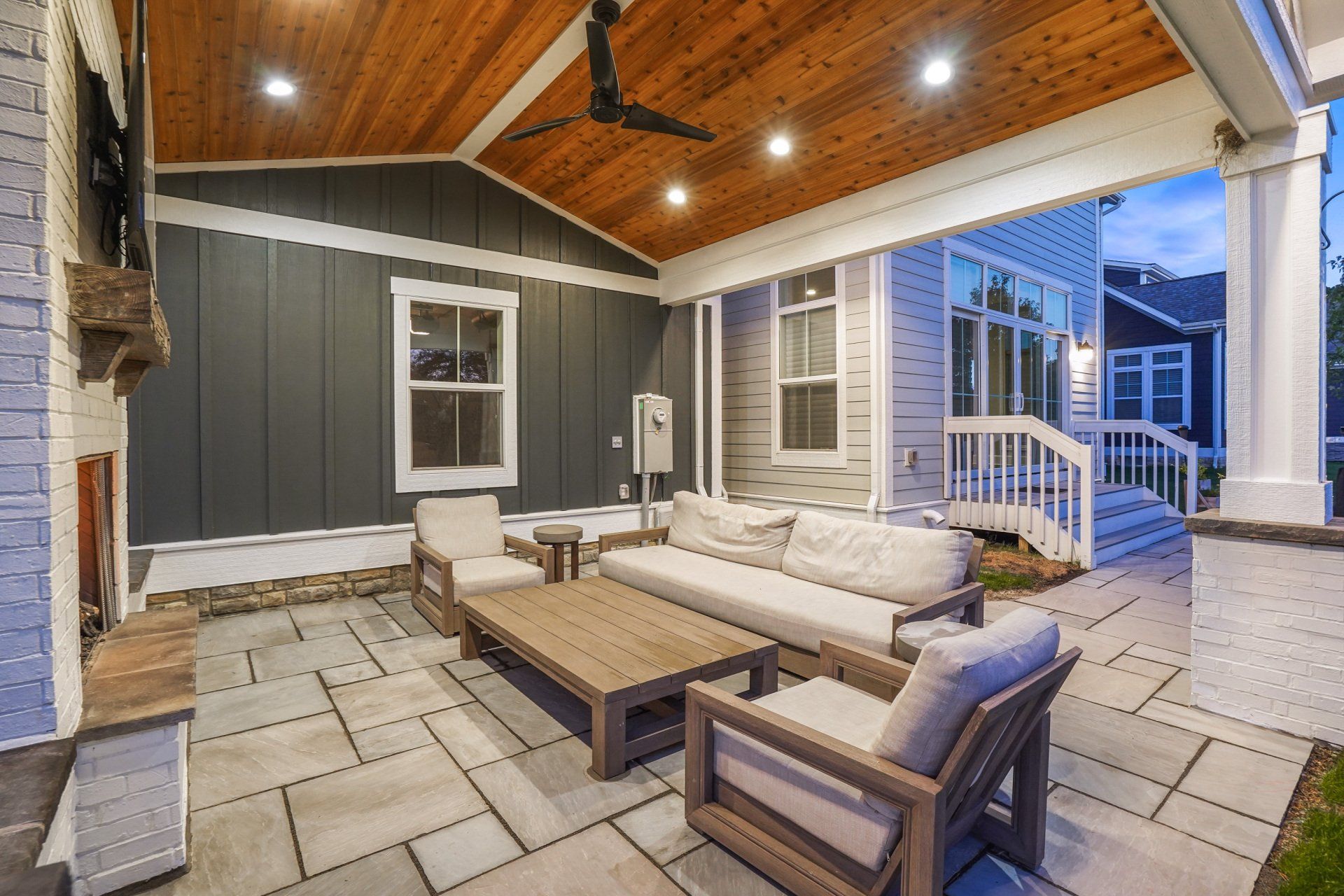Covered patio with outdoor sectional seating, coffee table, and stone fireplace under a wood ceiling.