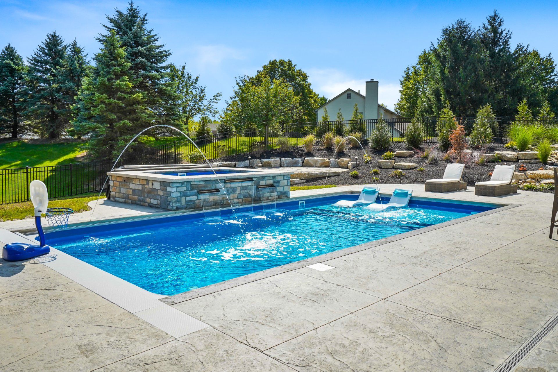 Backyard swimming pool with blue water, stone waterfall, and lounge chairs under a sunny sky