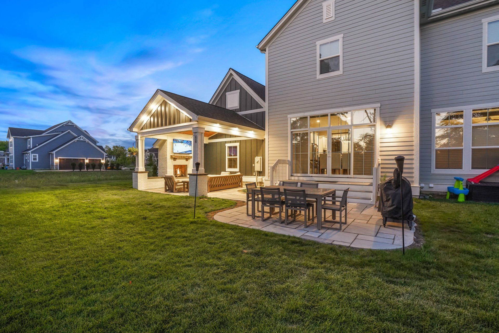 Backyard patio with outdoor dining set and grill beside a house at dusk