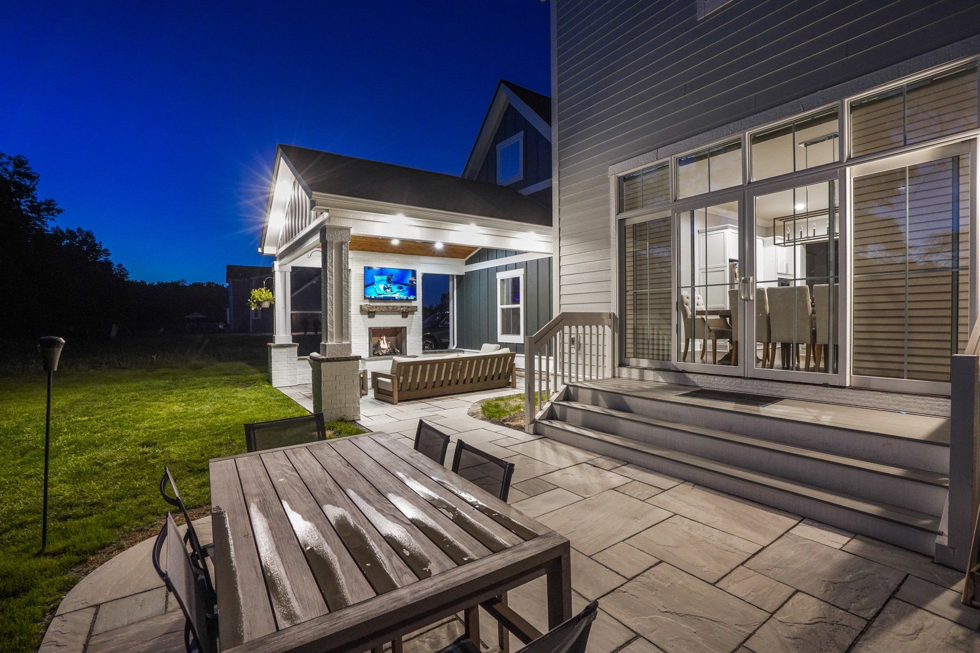Modern patio at dusk with outdoor seating, lit house exterior, and sliding glass doors
