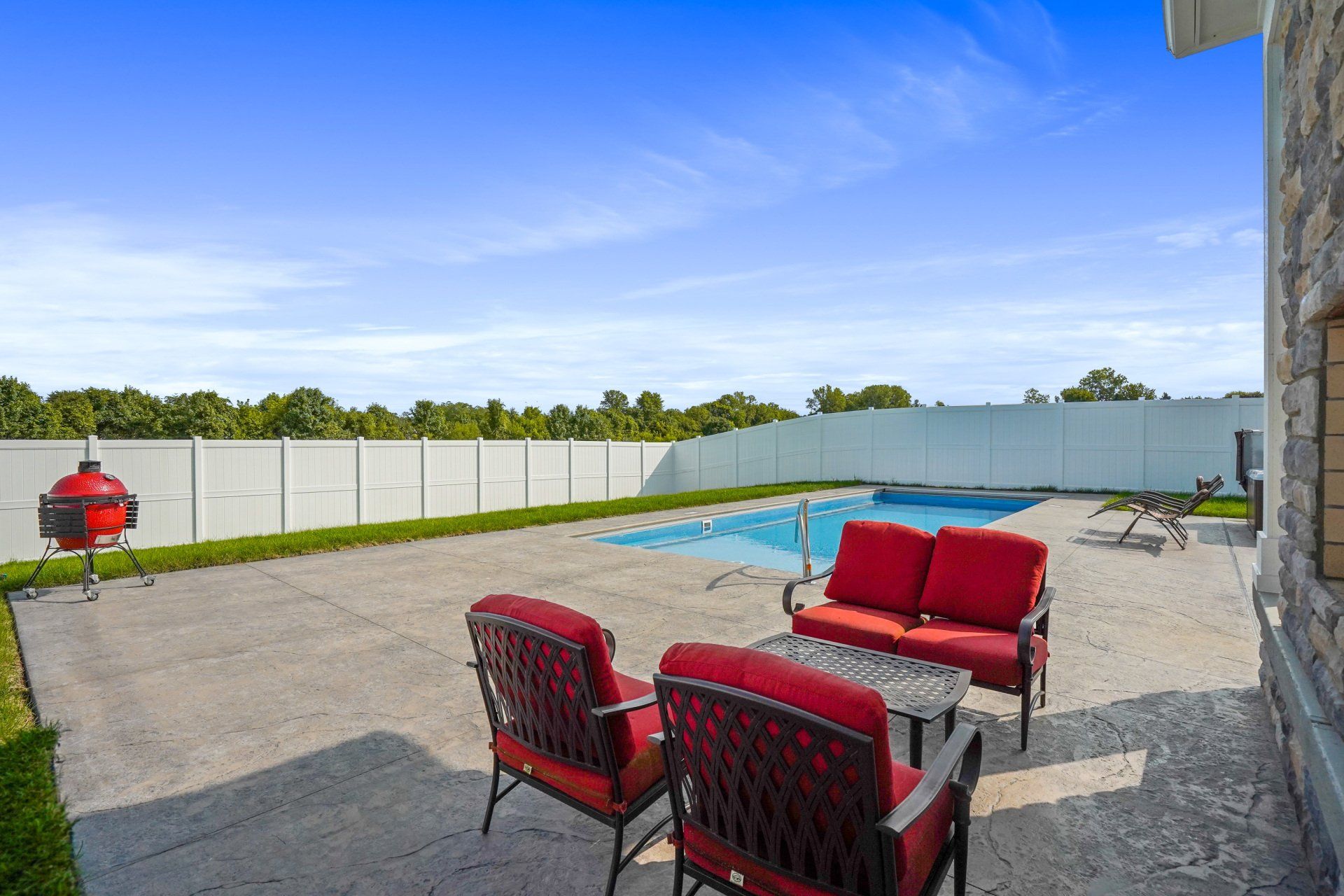 Patio with red outdoor furniture, grill, and a backyard pool under a bright blue sky