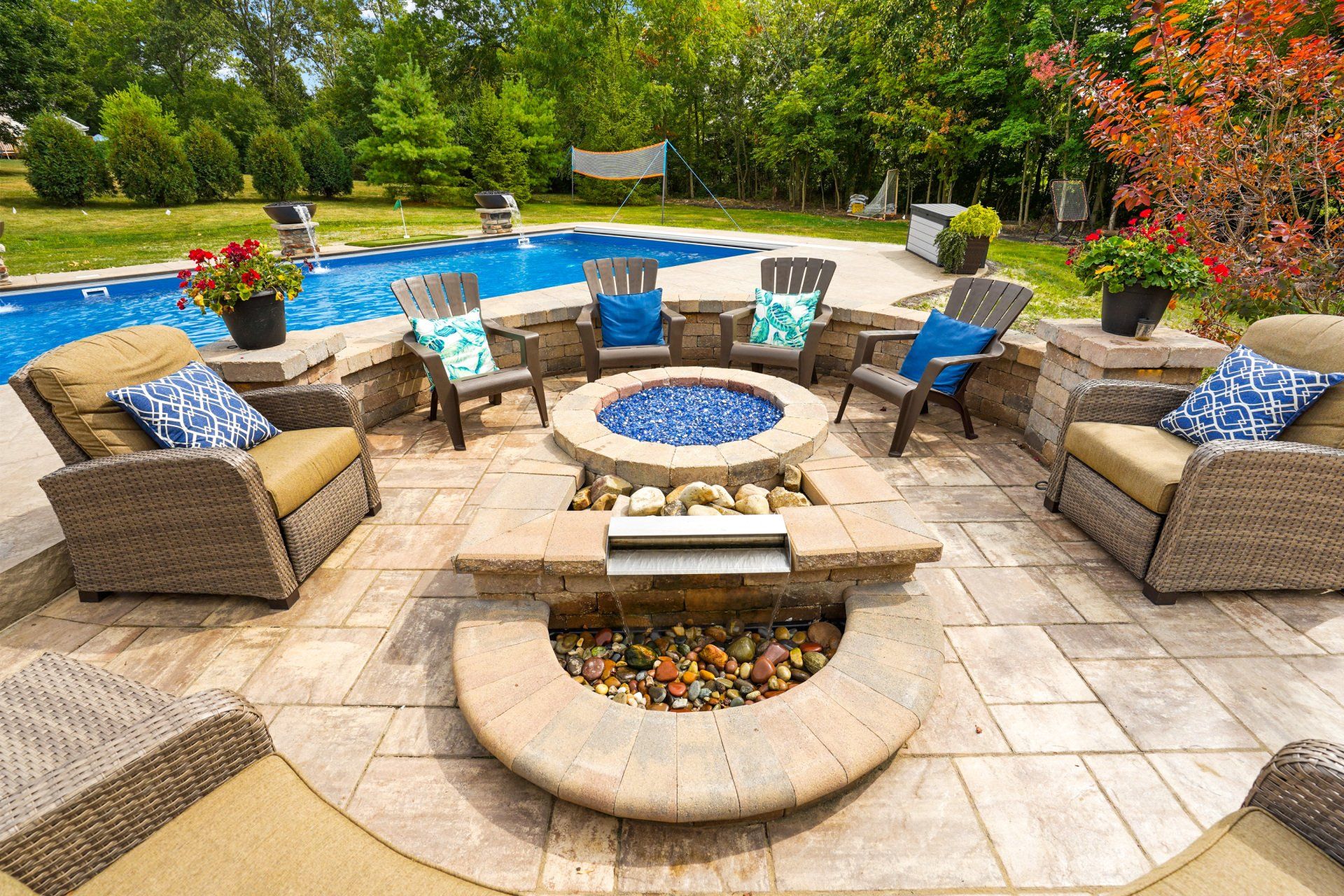 Backyard patio with wicker seating around a fire pit beside a blue swimming pool