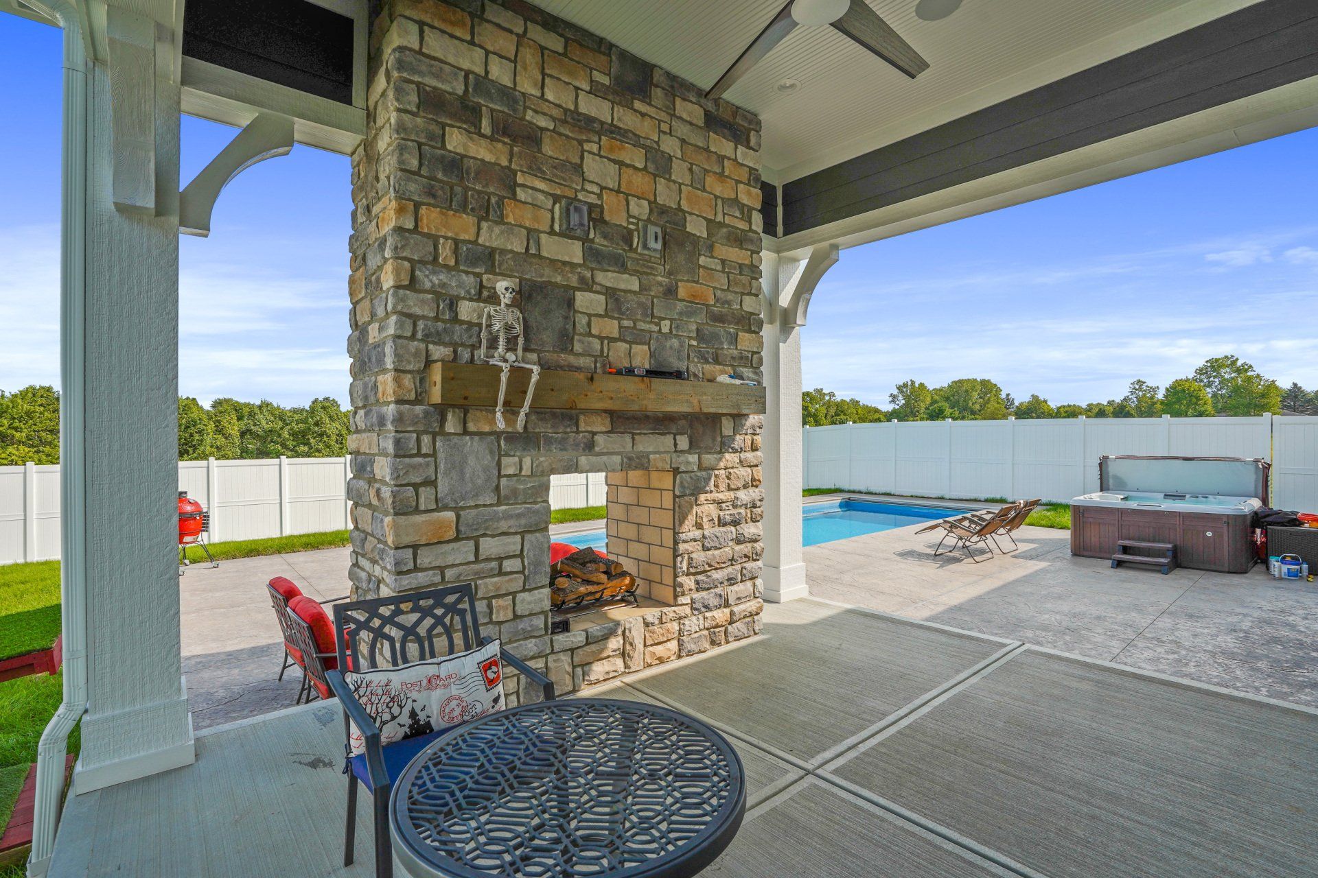 Covered patio with stone fireplace, seating, and a view of the pool and backyard