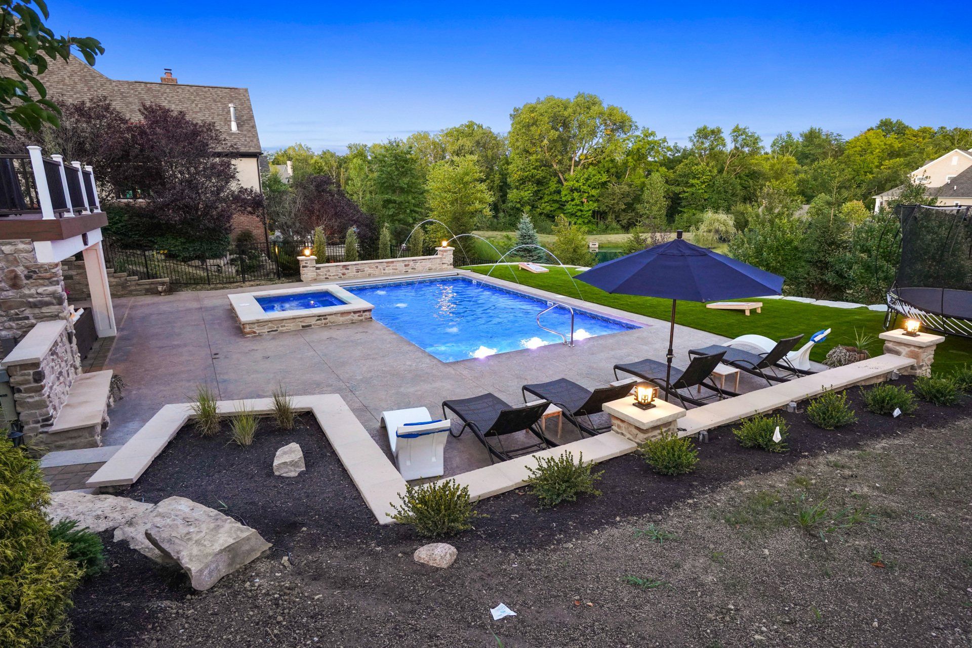 Modern backyard pool patio with lounge chairs, blue umbrellas, and stone landscaping