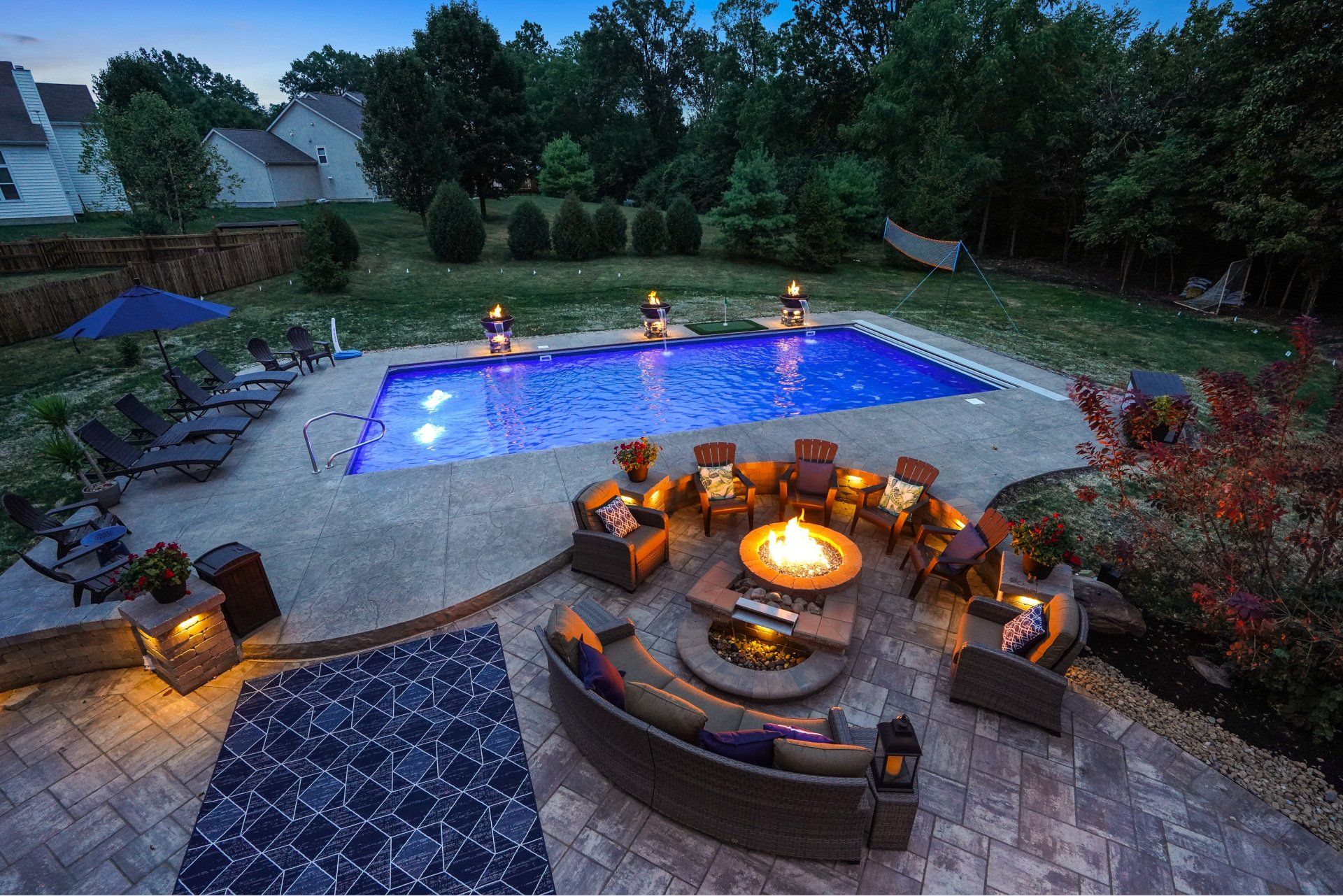 Backyard patio with lit fire pit seating and an illuminated swimming pool at dusk