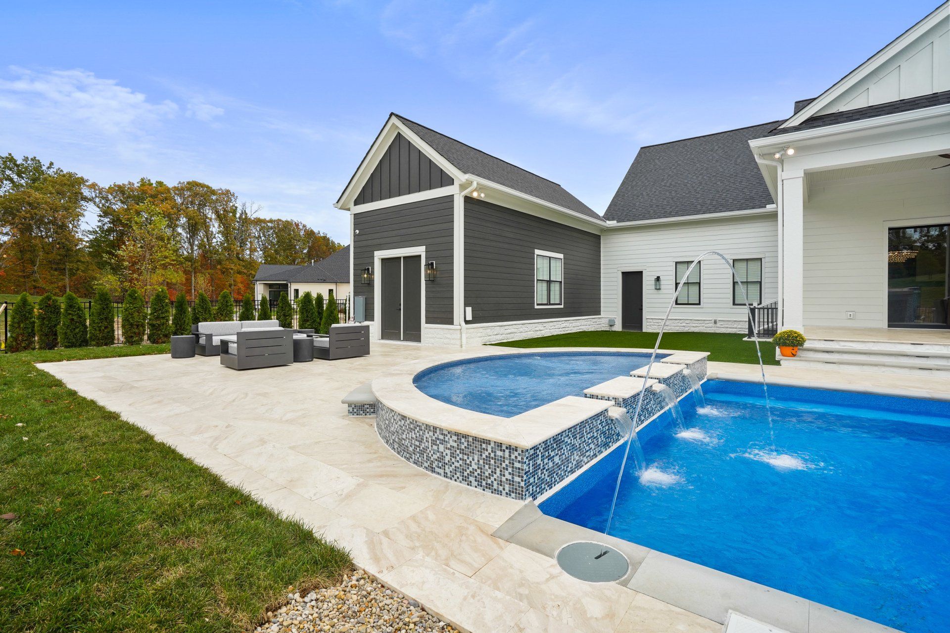 Modern backyard with a swimming pool, hot tub, patio seating, and gray house exterior