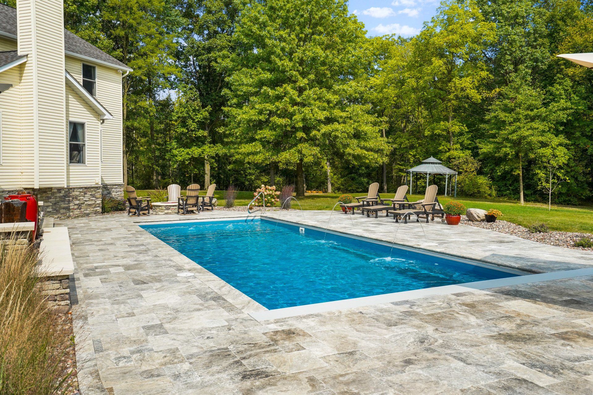 Backyard swimming pool with stone patio, lounge chairs, and trees in bright daylight