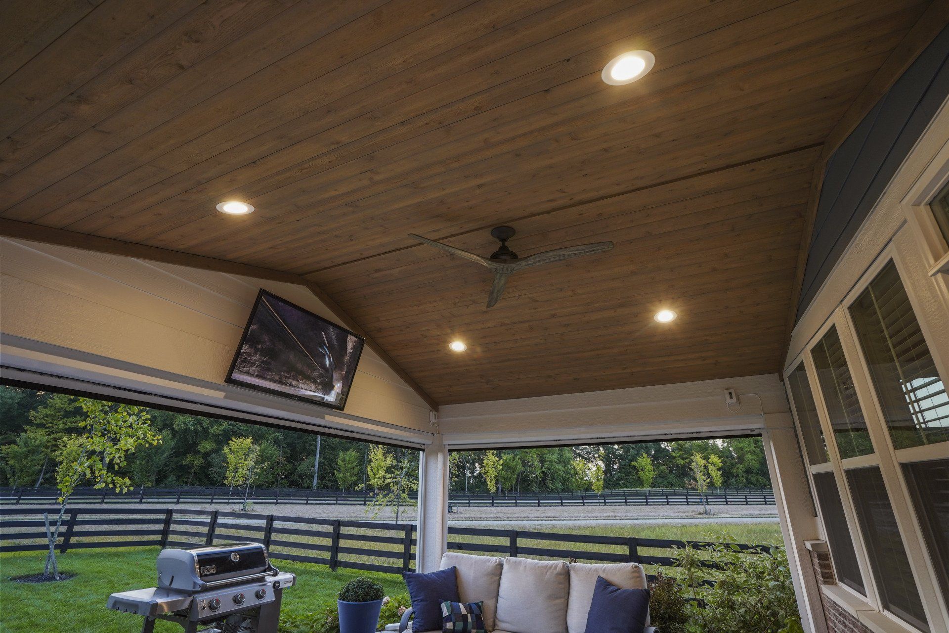 Covered patio with wood ceiling, recessed lights, seating, and a view of a fenced yard.