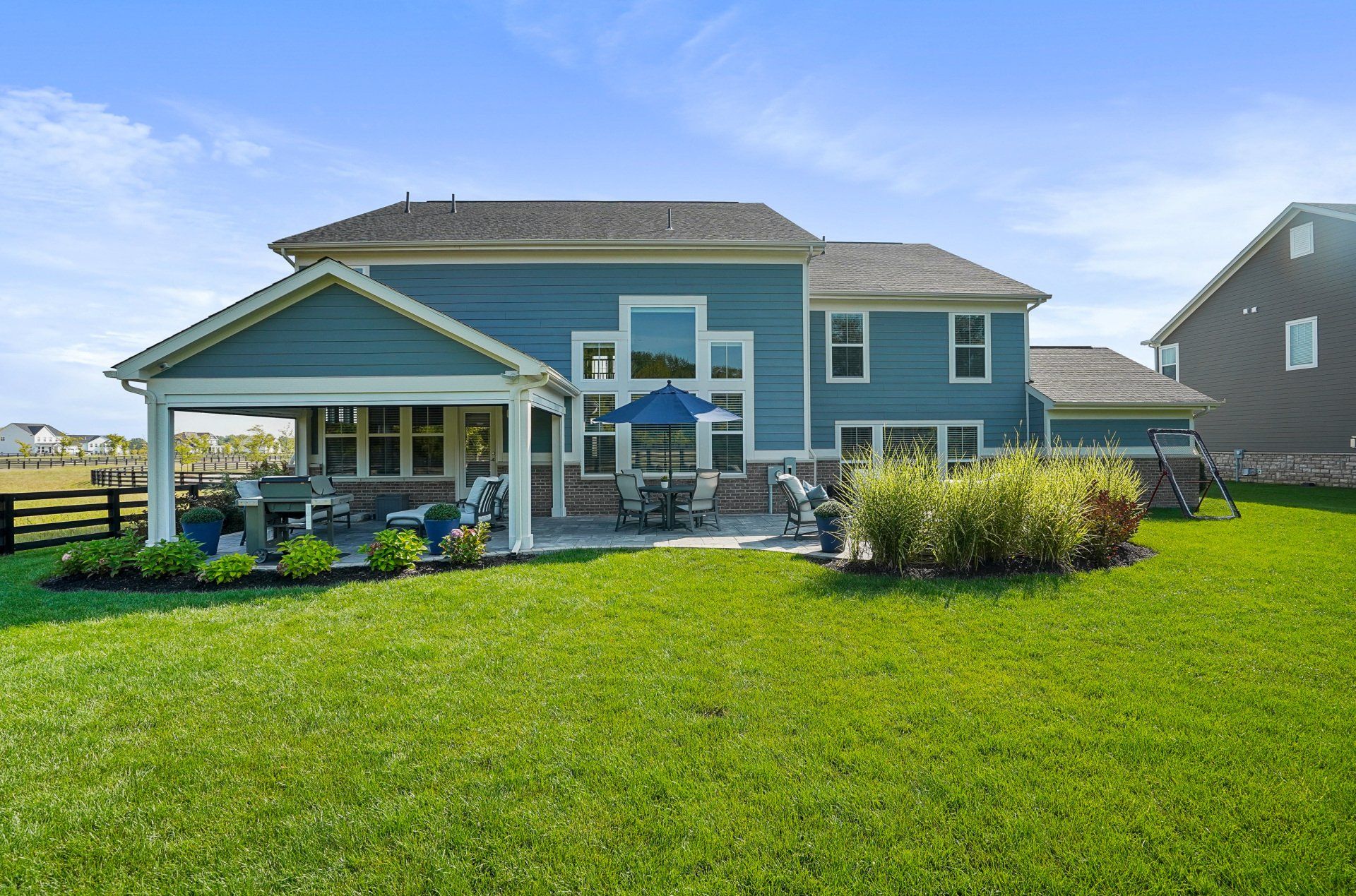 Blue two-story house with covered patio and large green backyard under a bright sky