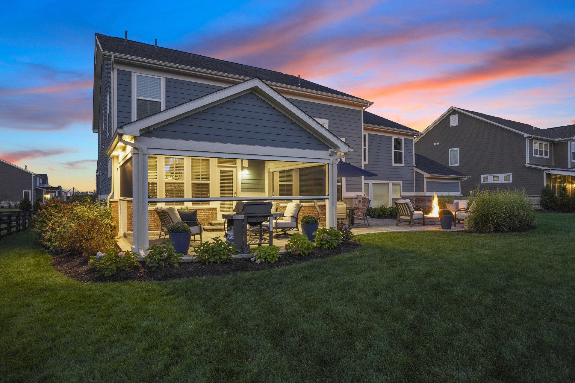 Suburban house with a lit covered patio at sunset and a grassy backyard
