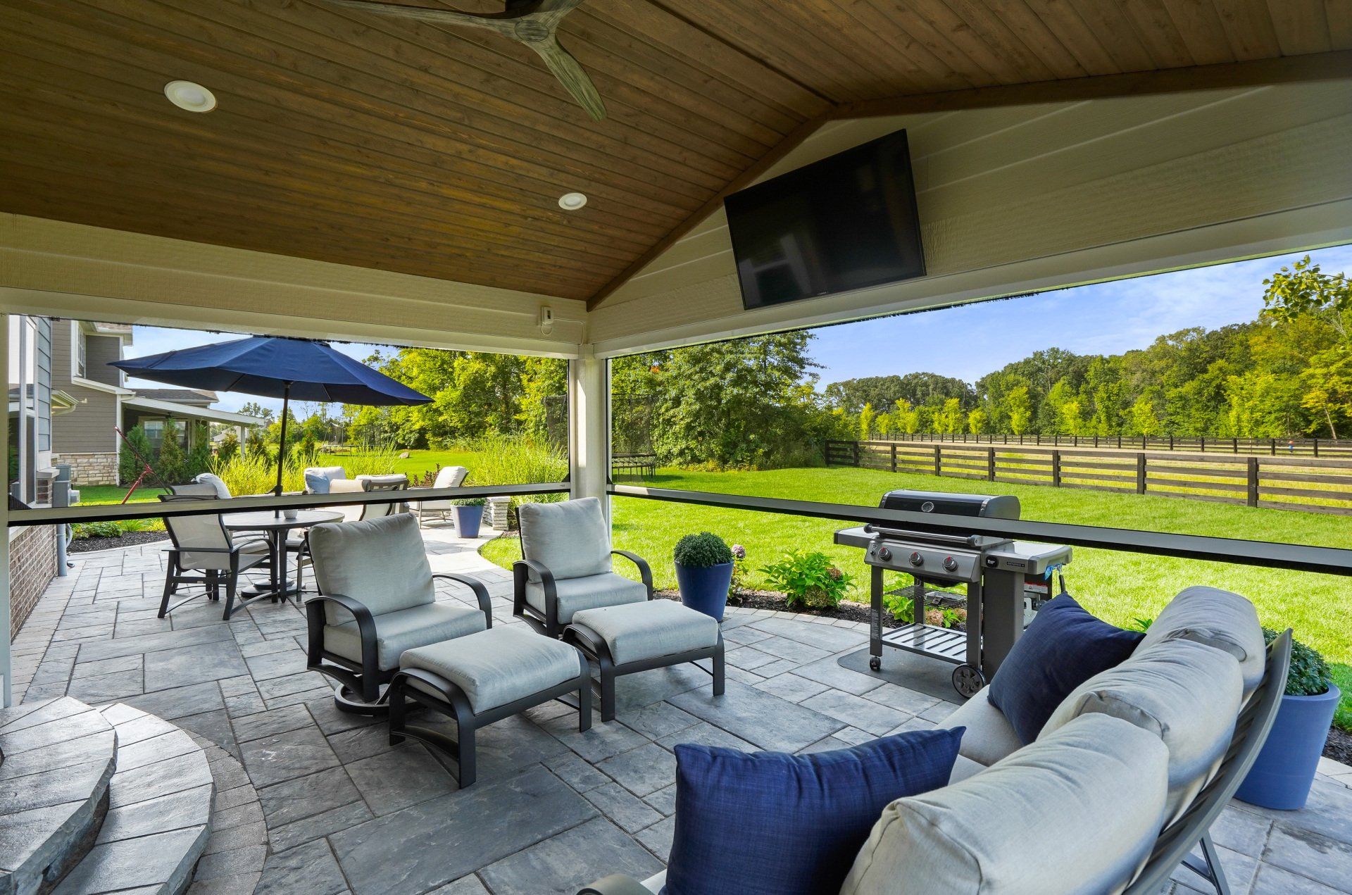 Covered patio with cushioned chairs and table overlooking a green lawn and fence