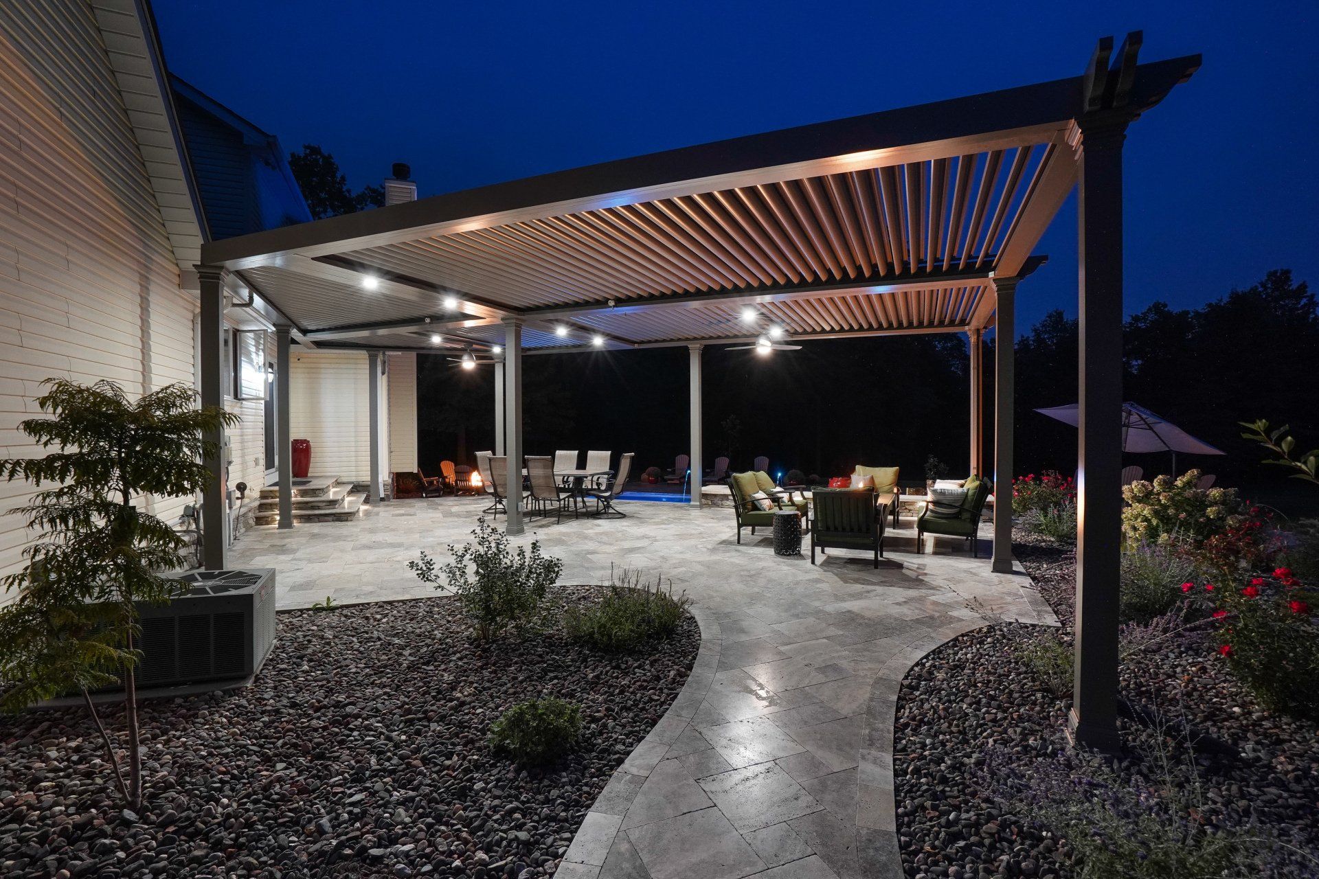 Modern patio with pergola lighting, curved stone path, and outdoor seating at dusk