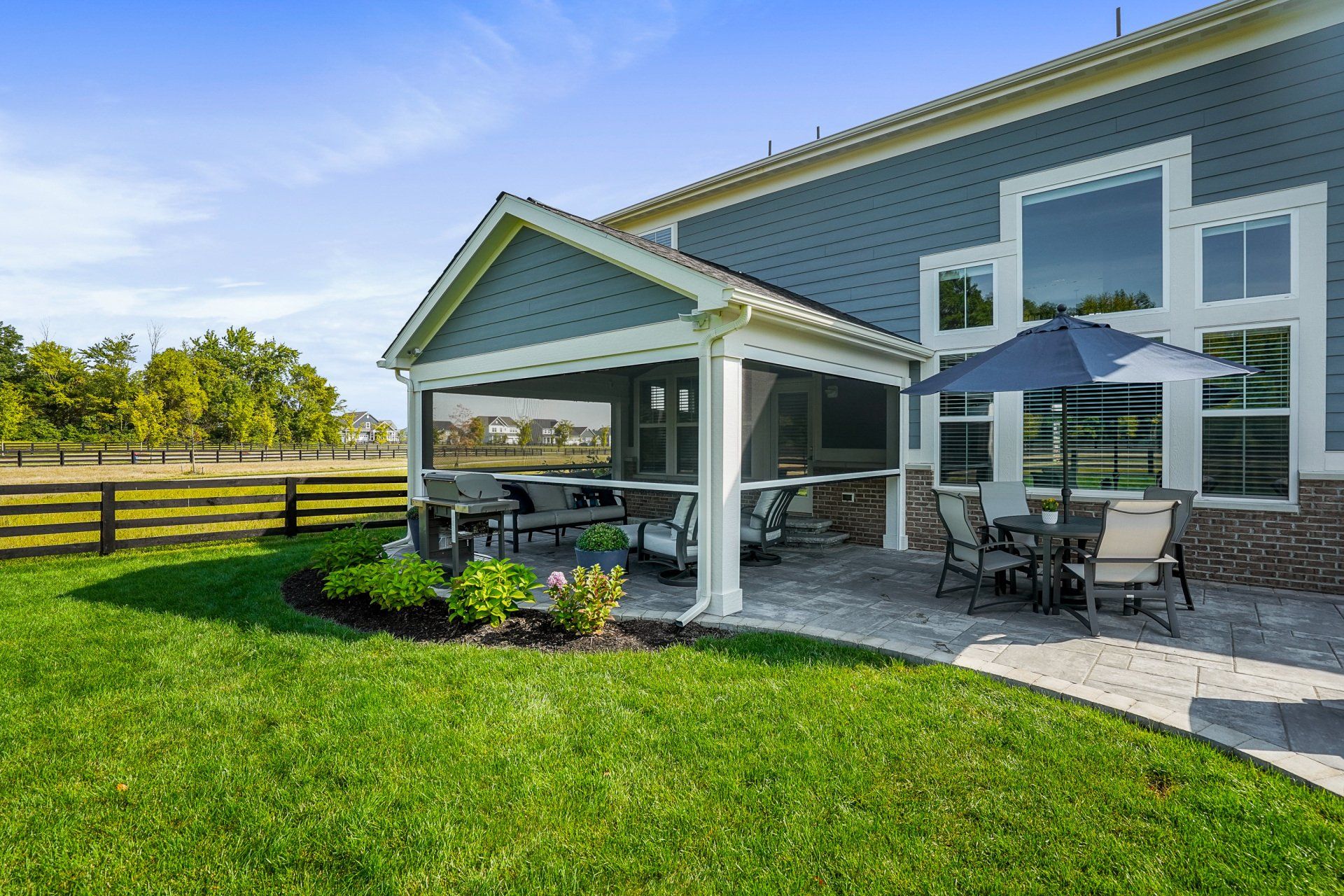 Covered patio with outdoor dining set and umbrellas beside a blue house and green lawn