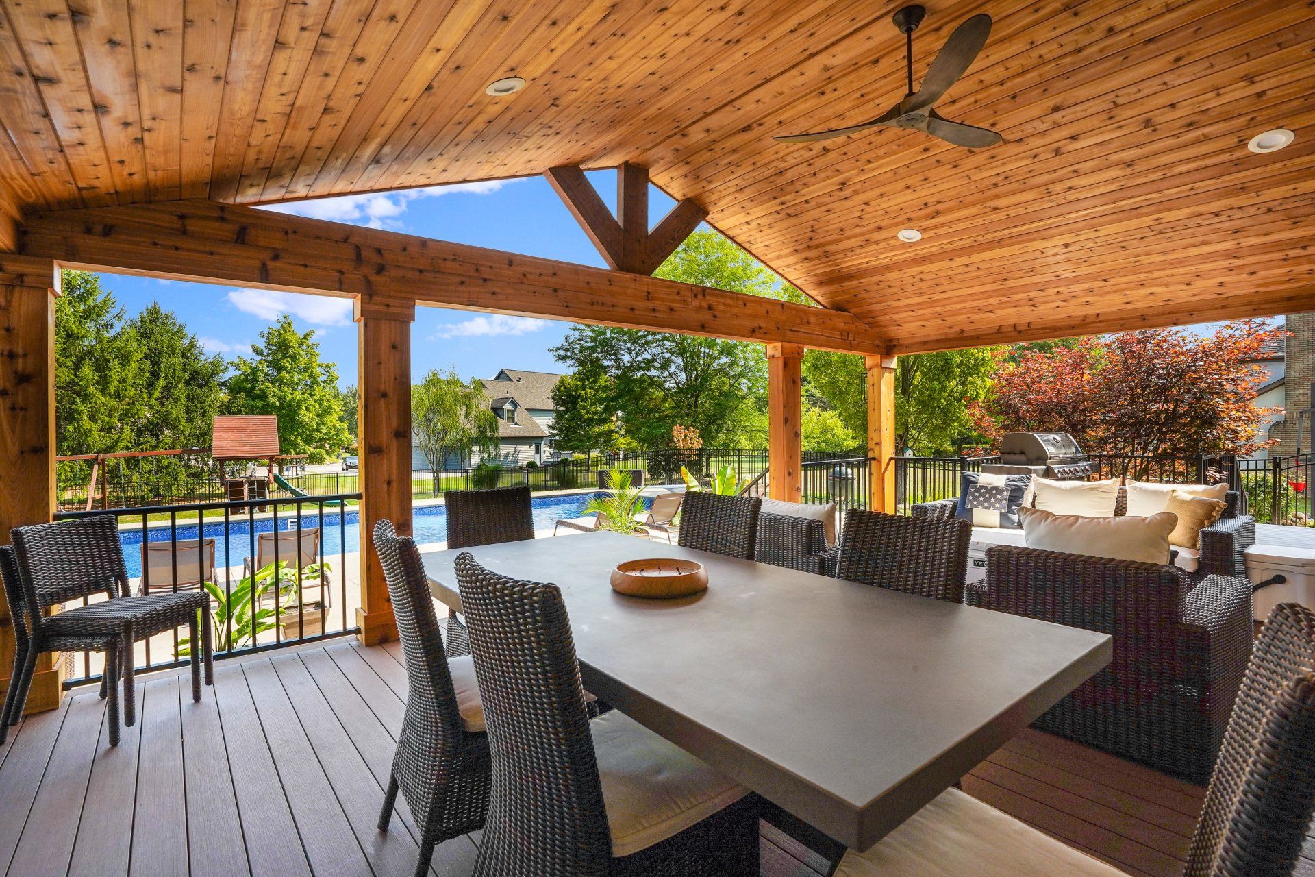 Covered patio dining area with wicker seating and pool view under a wooden pergola