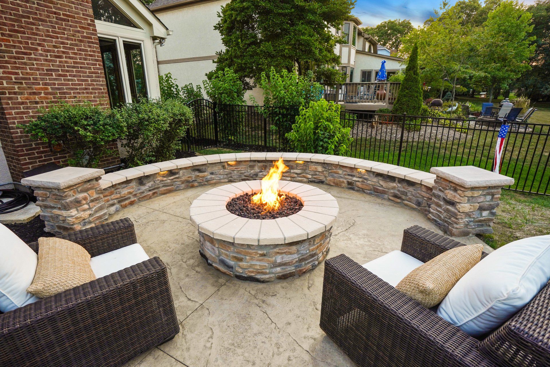 Outdoor patio with wicker chairs around a stone fire pit in a landscaped backyard.