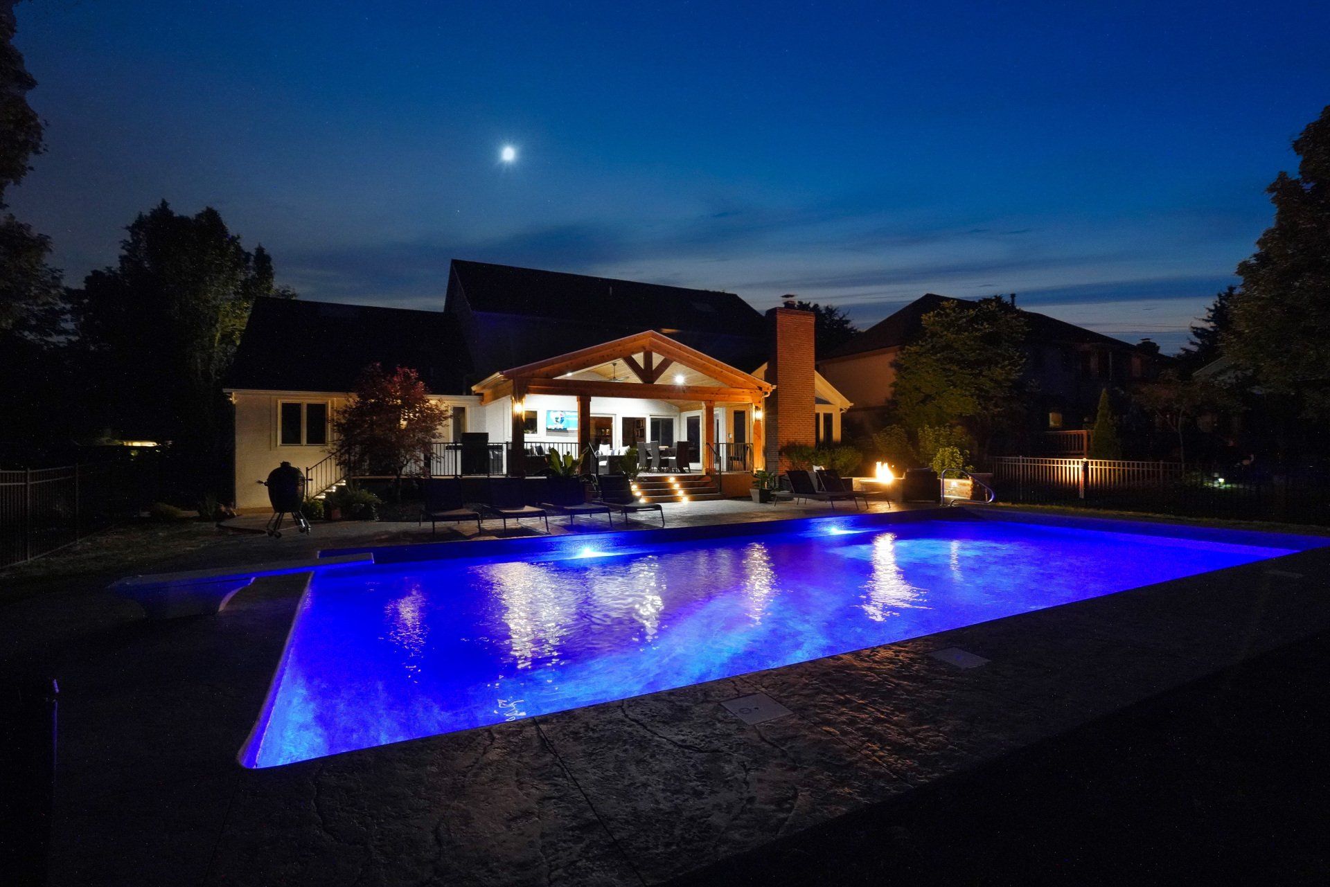 Nighttime backyard with lit house and glowing blue swimming pool