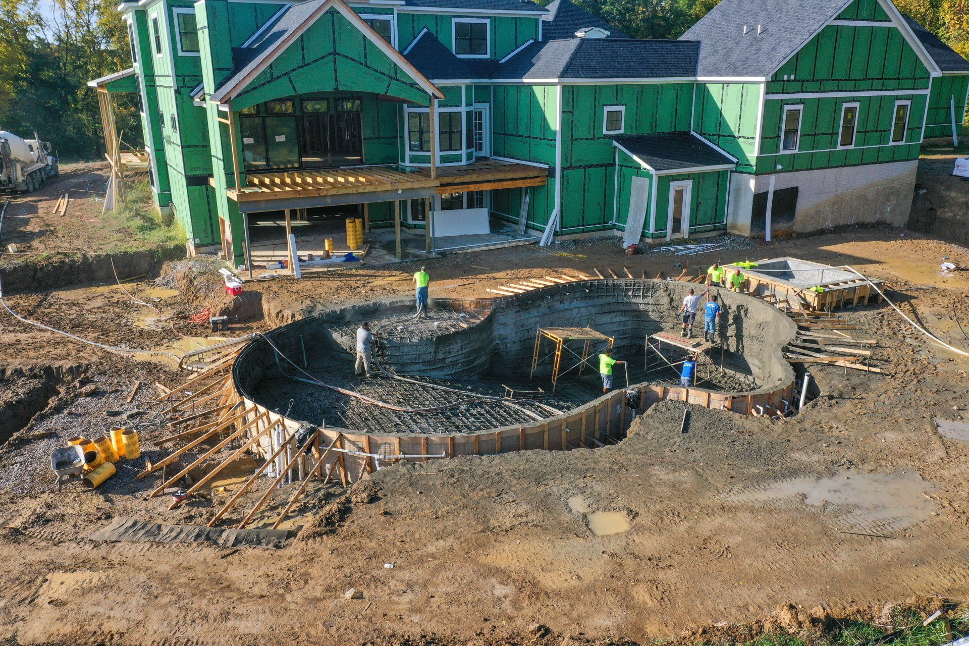 Construction site with a circular stone foundation in front of green houses and workers nearby