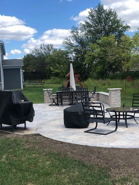 Outdoor patio with black chairs, tables, umbrella, and fire pit on a concrete slab beside a lawn and house