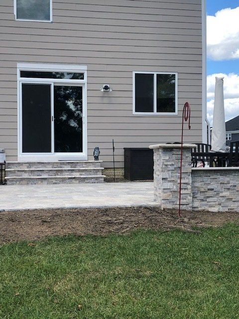 Back patio with sliding glass door, stone steps, and a small brick pillar beside a lawn