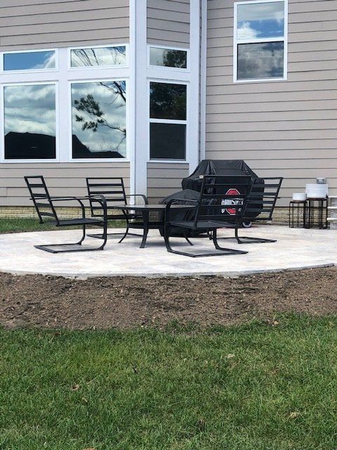Patio seating with black chairs and grill on a concrete patio beside a beige house