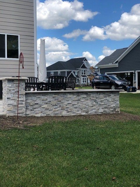 Brick patio wall with black railing beside a house, with neighboring homes and a parked truck in the background.