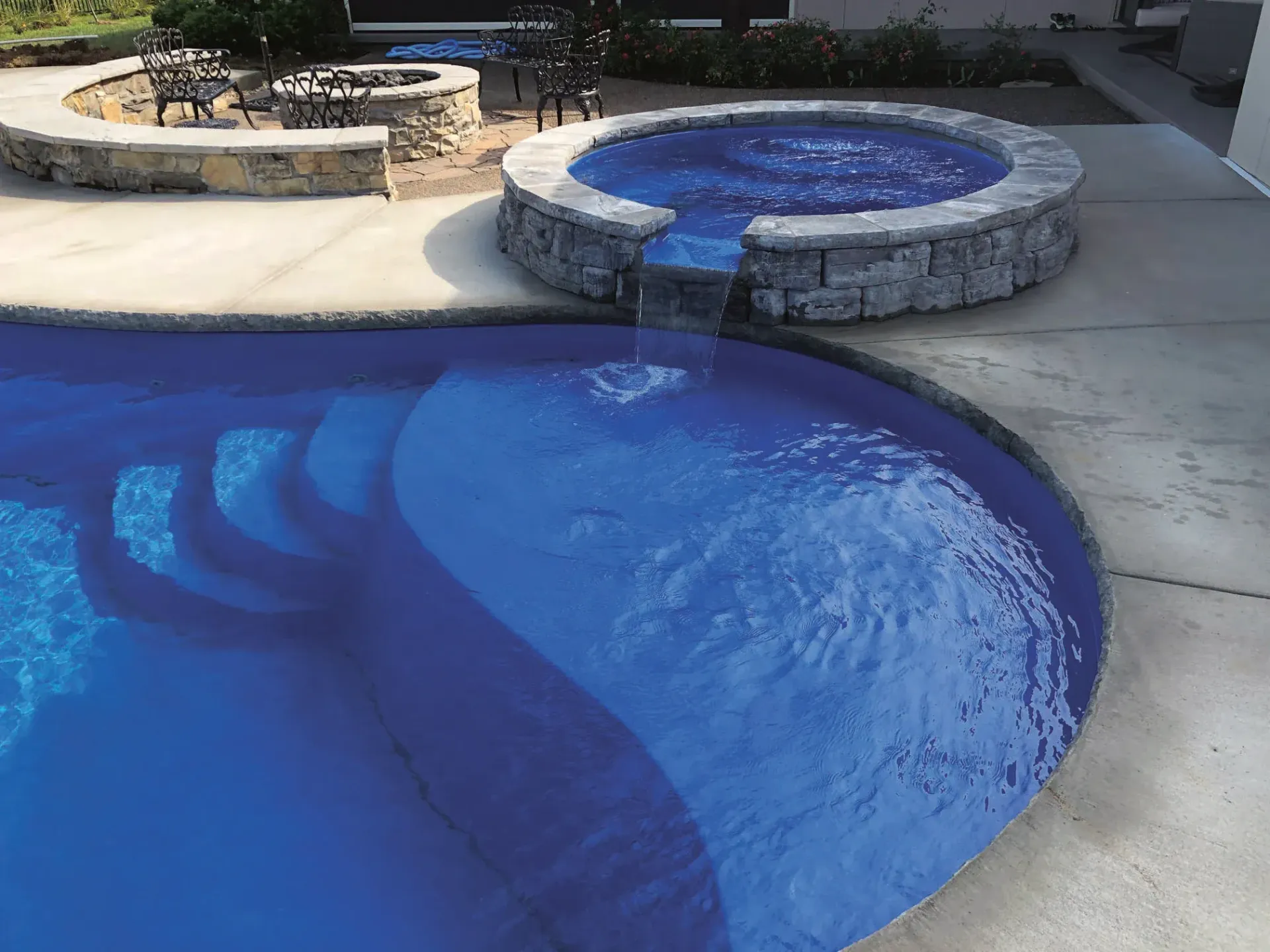 Backyard pool with blue water and a round raised spa beside it