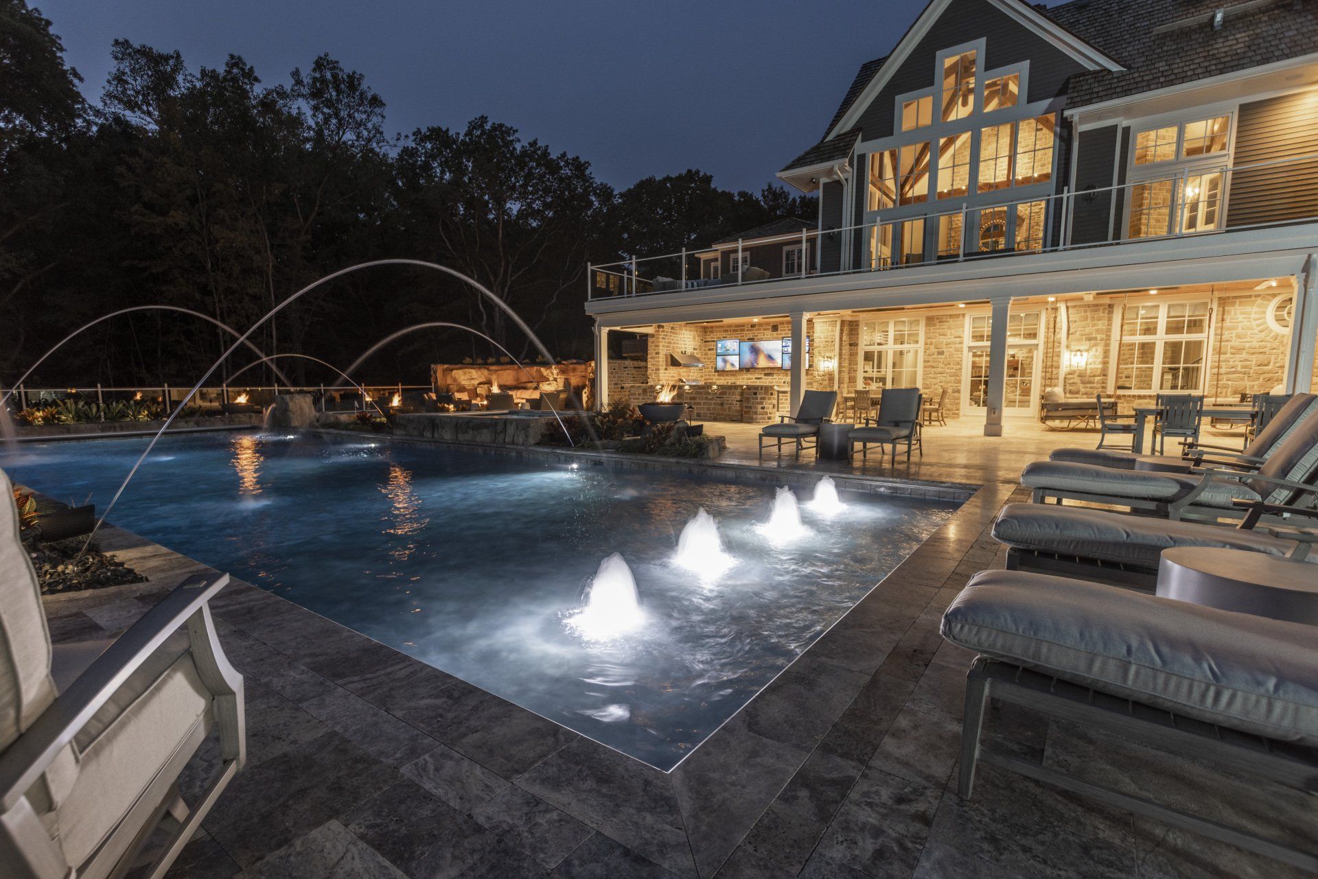 Nighttime resort pool with illuminated fountains beside a warmly lit lodge terrace