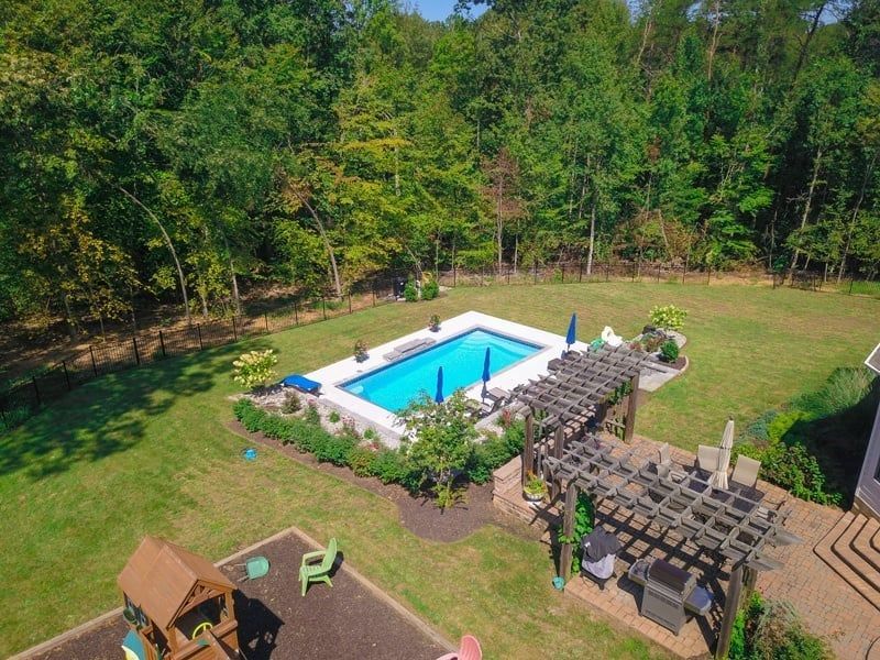 Backyard with a small blue swimming pool, patio furniture, and trees around the lawn.