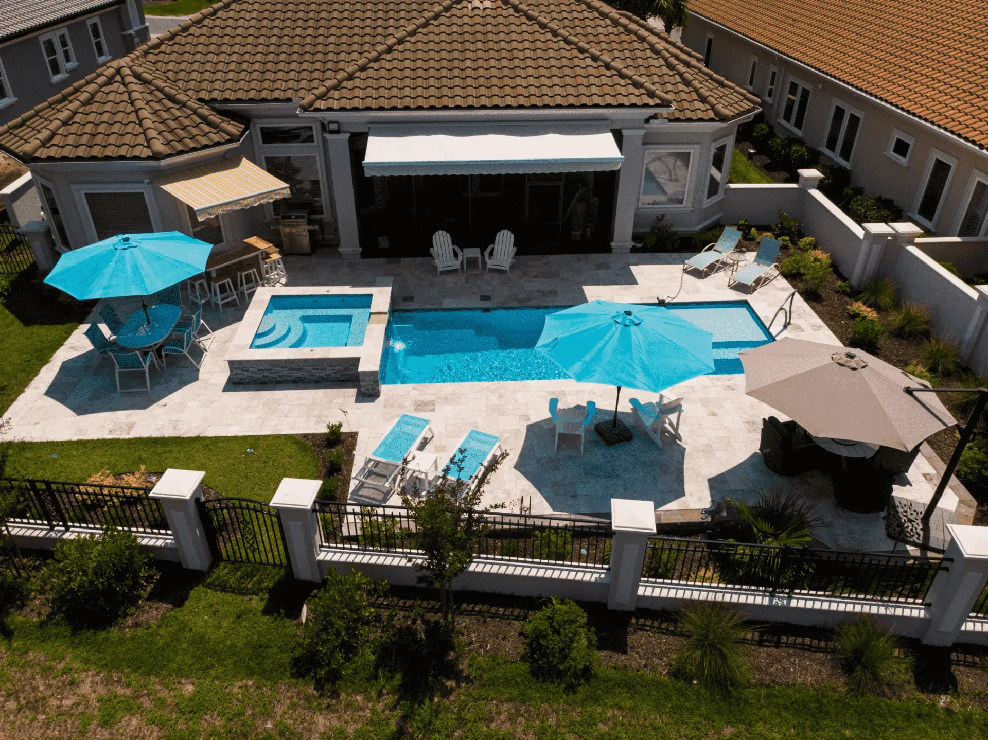 Luxury backyard patio with blue pool, hot tub, umbrellas, lounge chairs, and a covered outdoor seating area