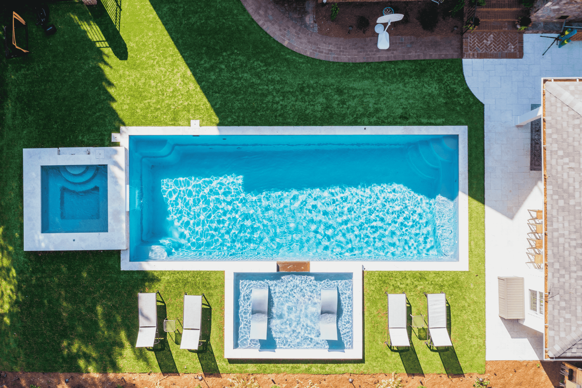 Aerial view of a backyard pool with hot tub, loungers, and patio seating around turquoise water