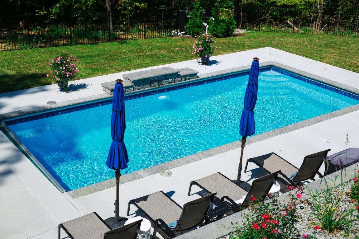 Rectangular outdoor swimming pool with blue water, umbrellas, lounge chairs, and flowers nearby