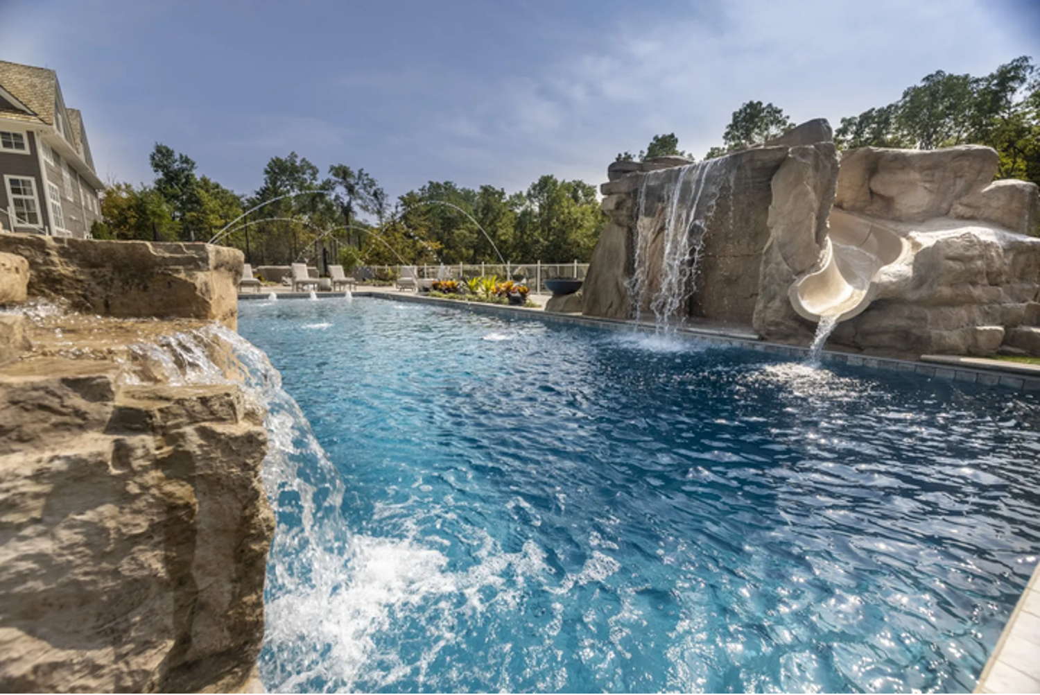 Resort pool with blue water, rock waterfall, and tan stone landscaping under a sunny sky