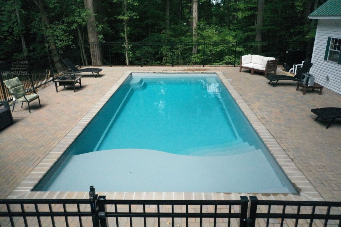Backyard patio with a rectangular in-ground pool, surrounded by trees and lounge chairs